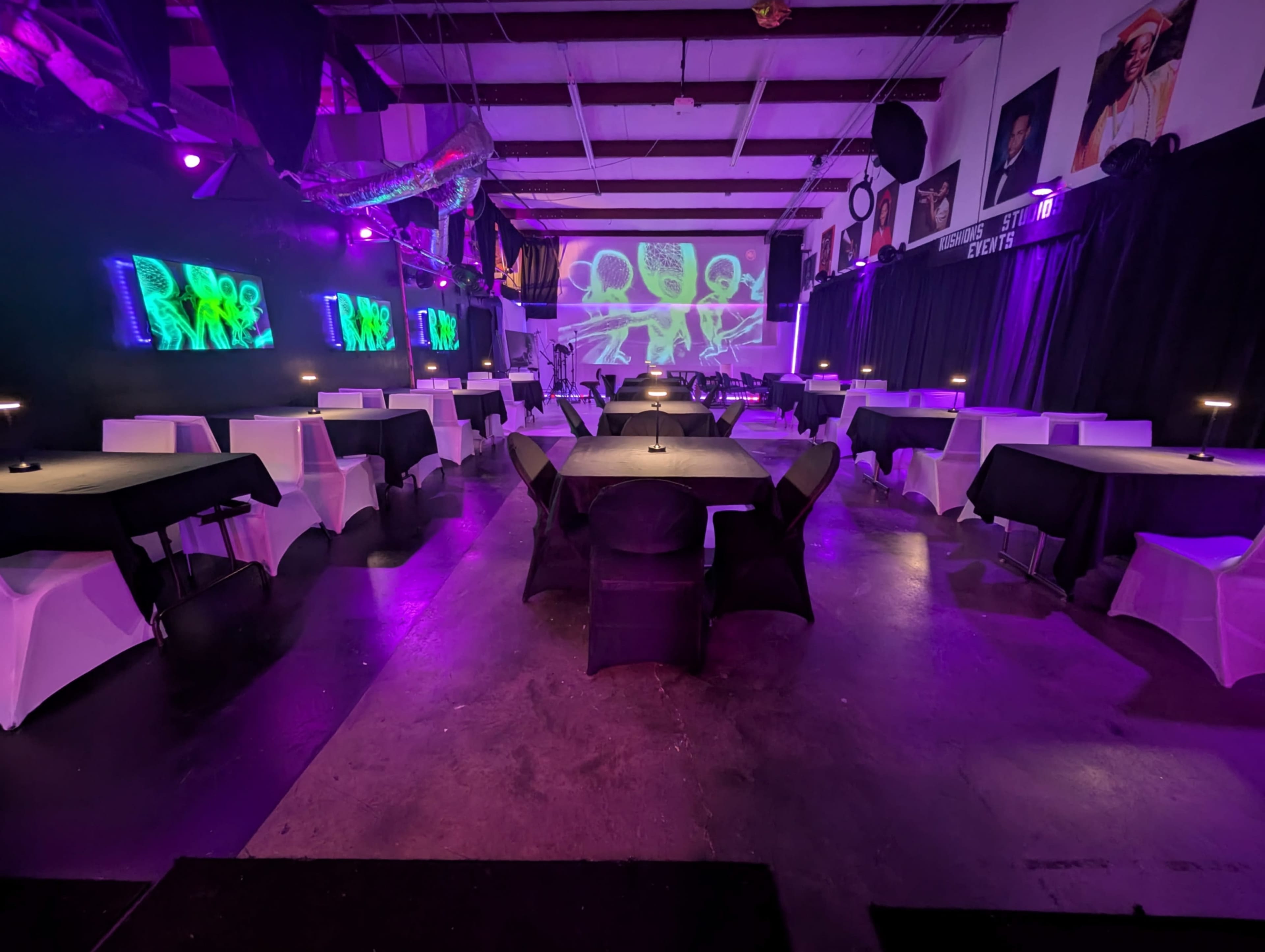 The image shows a spacious event venue with tables set for dining, illuminated by purple lighting and featuring projected graphics on a wall.
