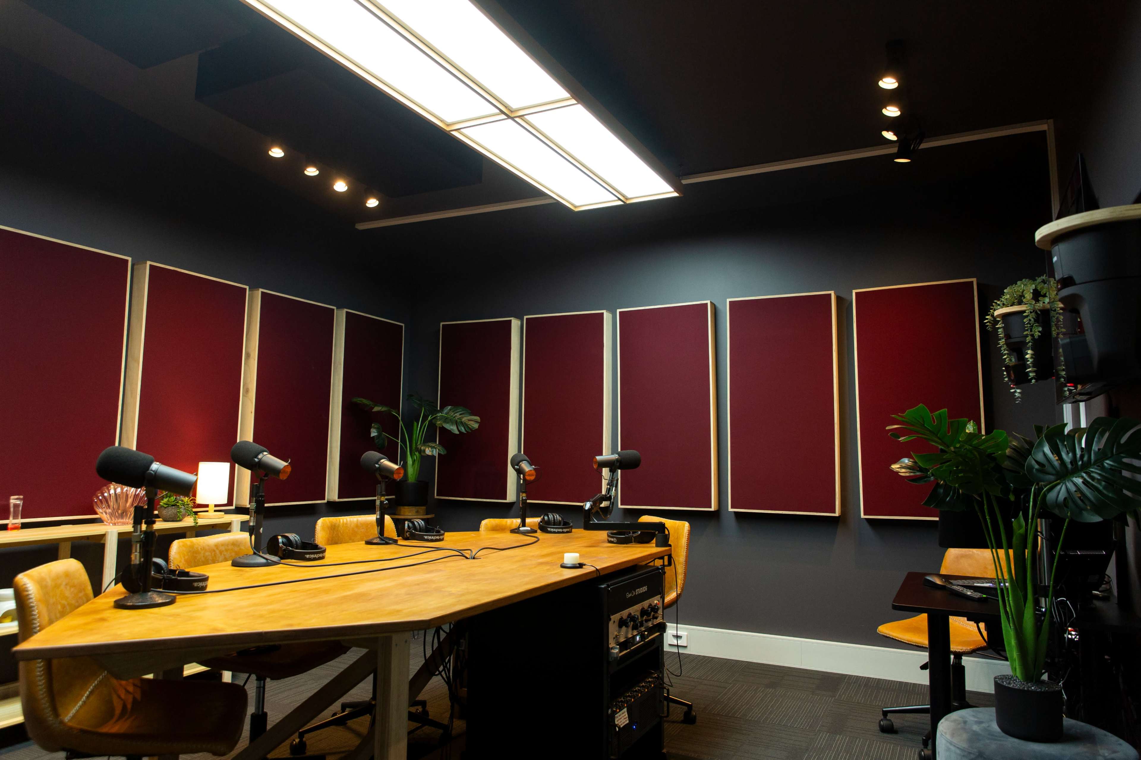 A modern podcast recording studio with a large wooden table, multiple microphones, and soundproofed walls.