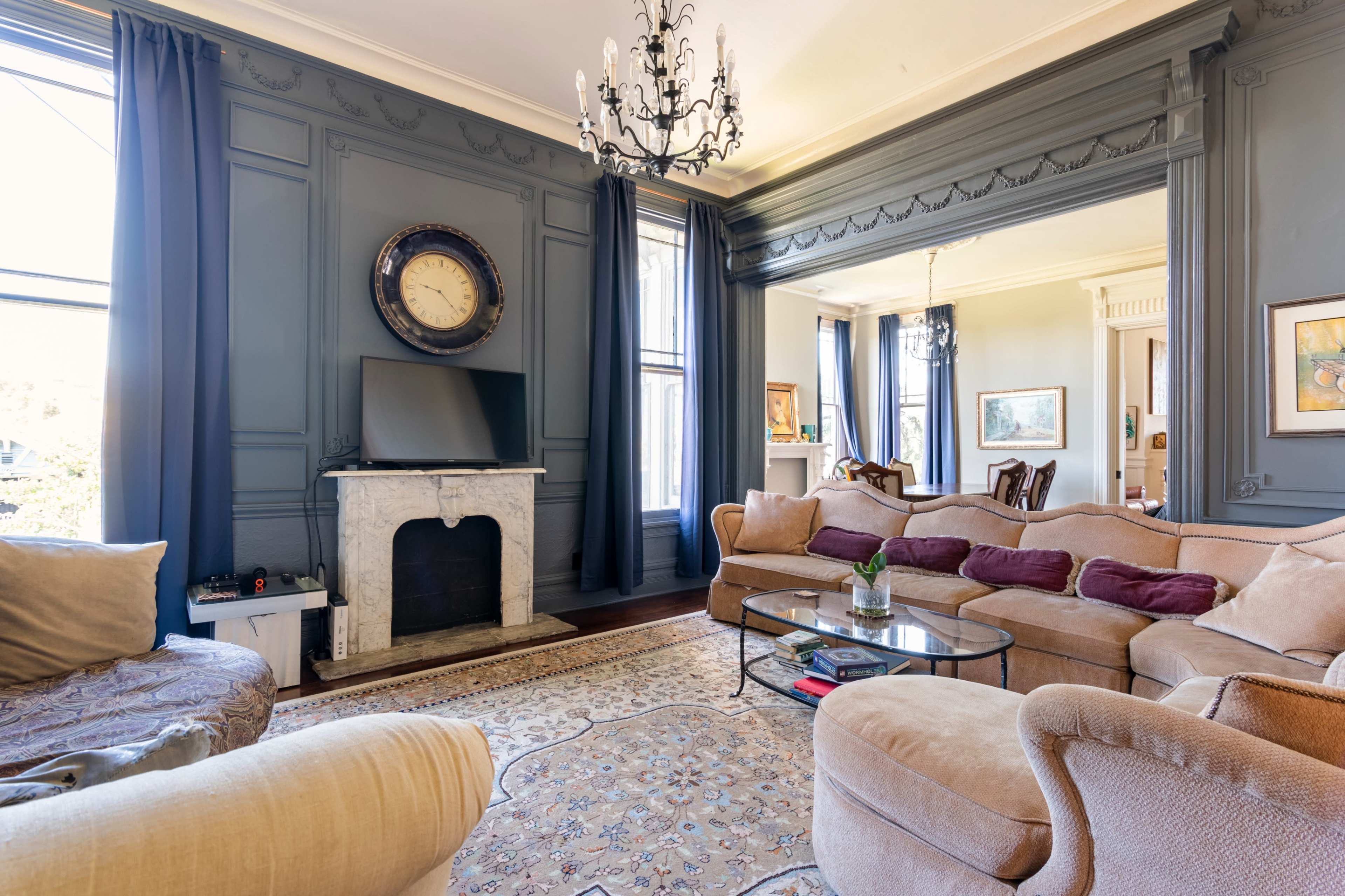 The living room features a chandelier, a wall-mounted television, a marble fireplace, and a large sectional sofa arranged around a glass coffee table.