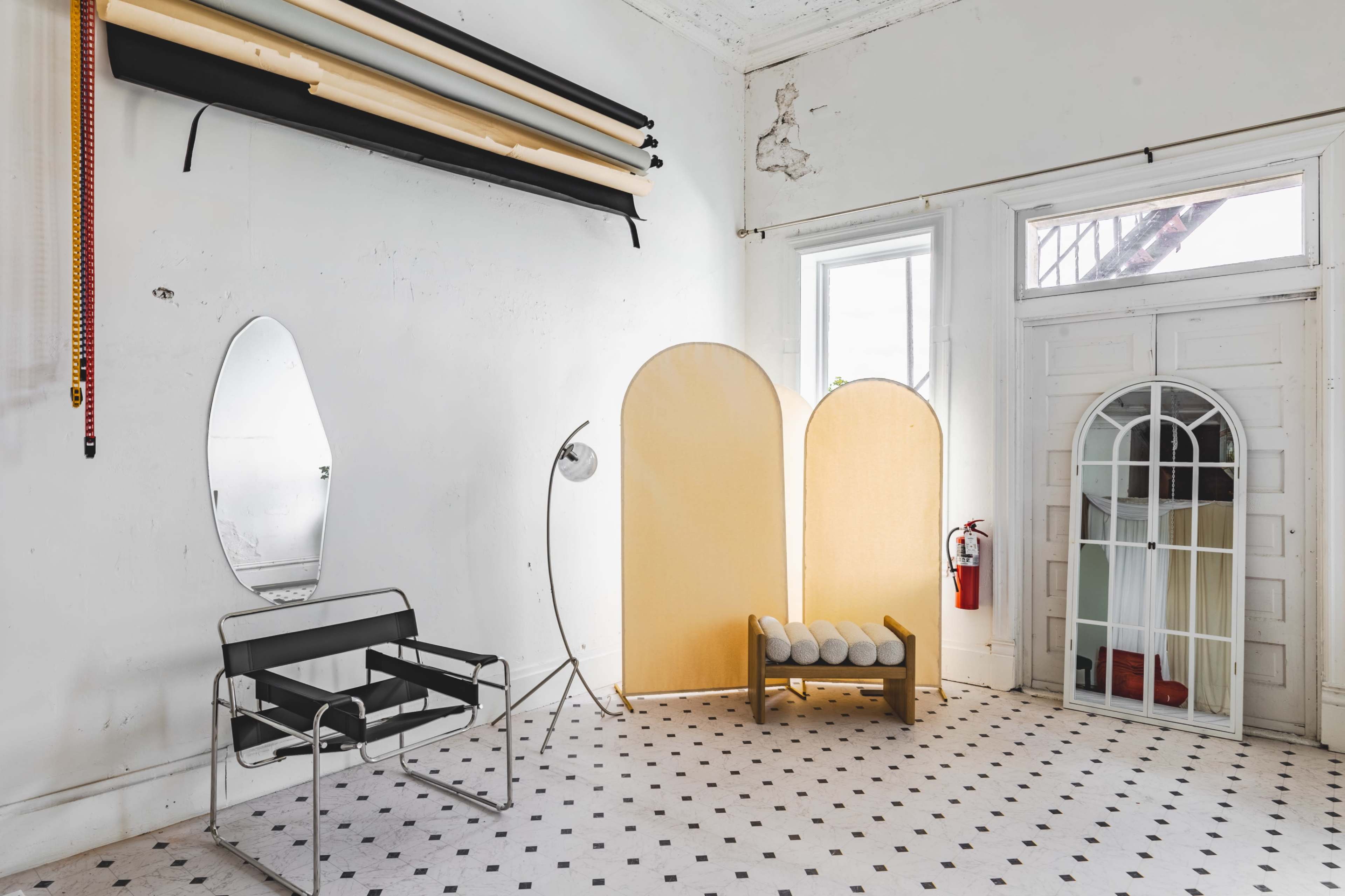 An interior space featuring a chair, backlit screens, a mirror, a lamp, and a decorative arch-shaped mirror against a patterned floor.