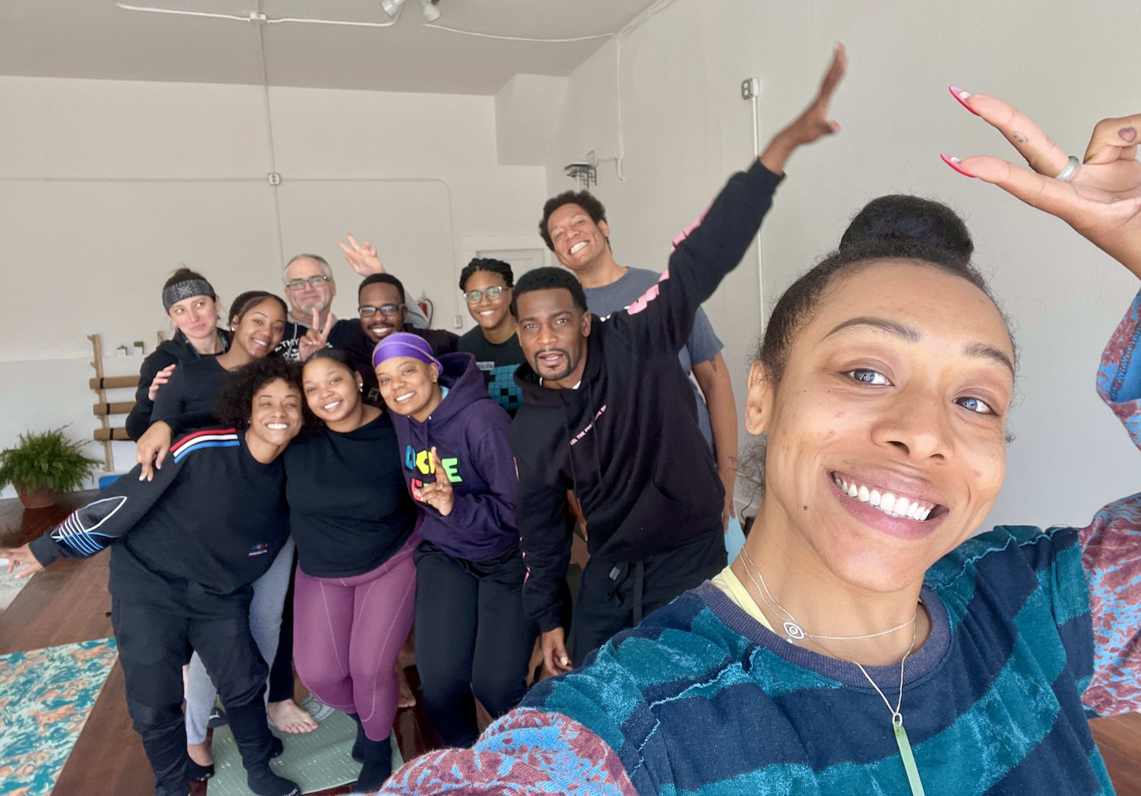 A group of eleven people poses together in a well-lit room, smiling and making playful gestures.