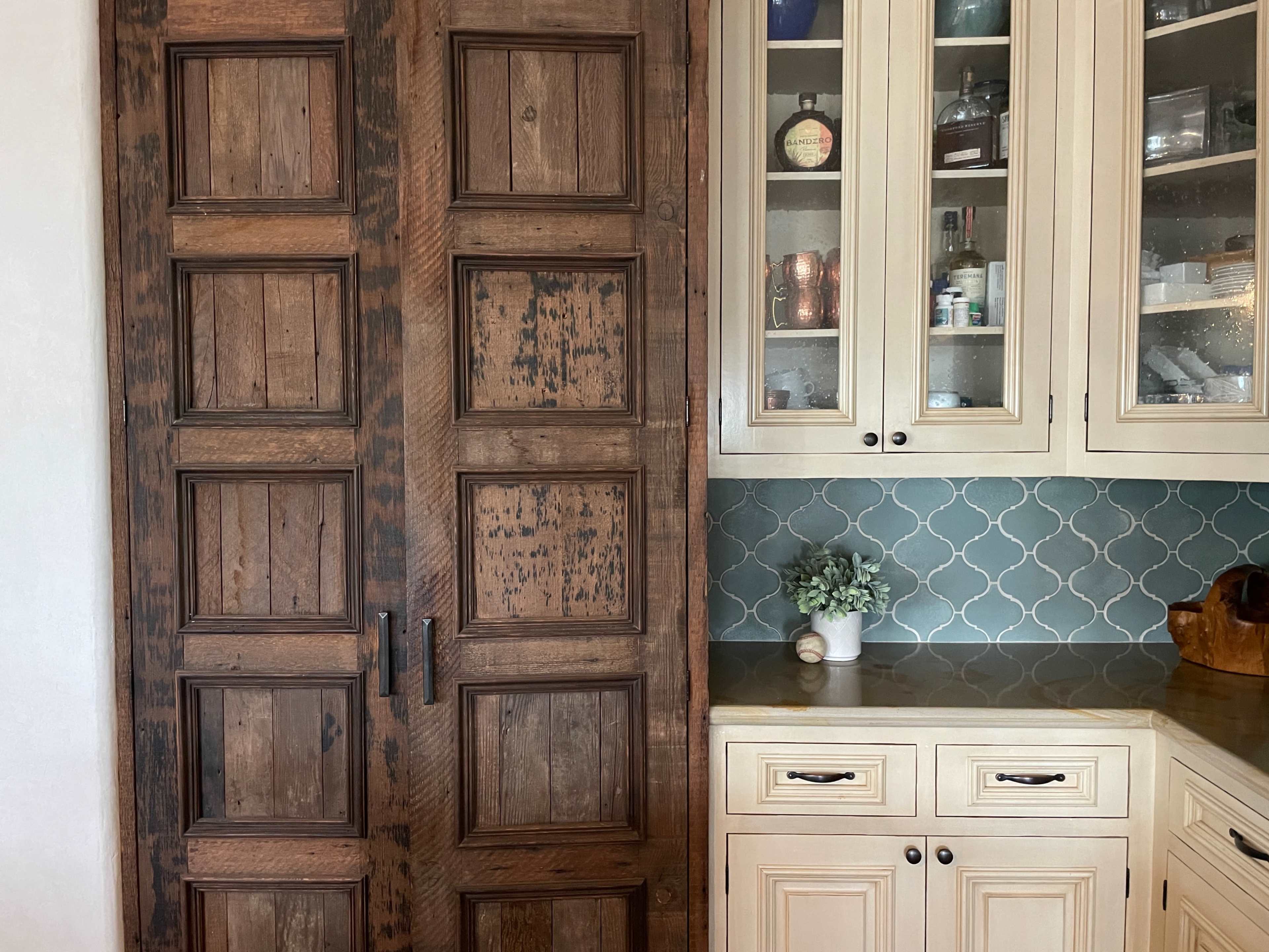 A wooden sliding door beside a set of glass-front cabinets with a teal tiled backsplash.