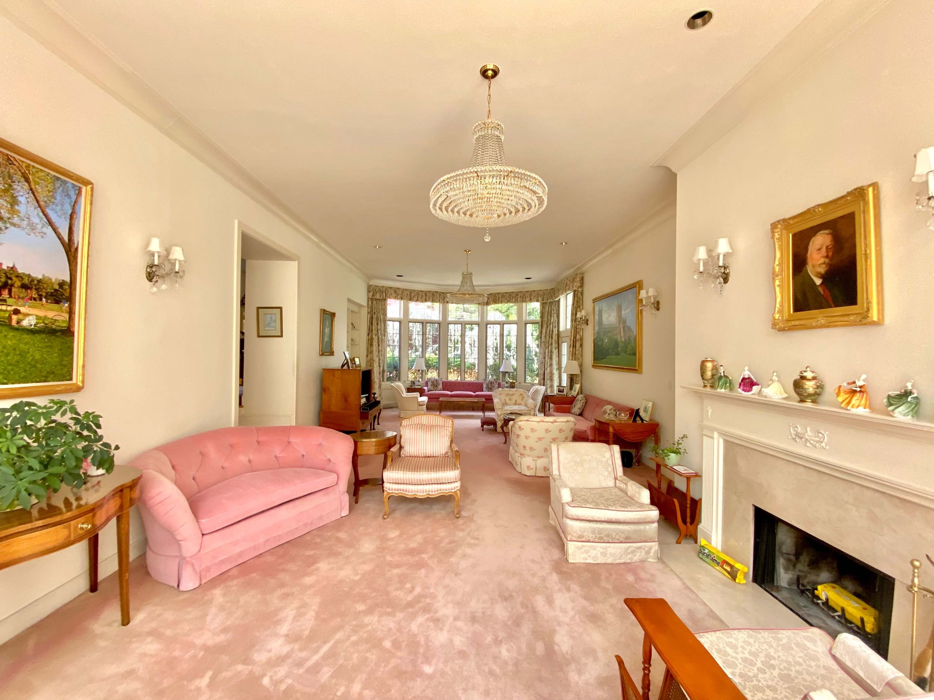 A spacious living room featuring pink and light-colored furniture, large windows, and various decorative items on the walls and shelves.