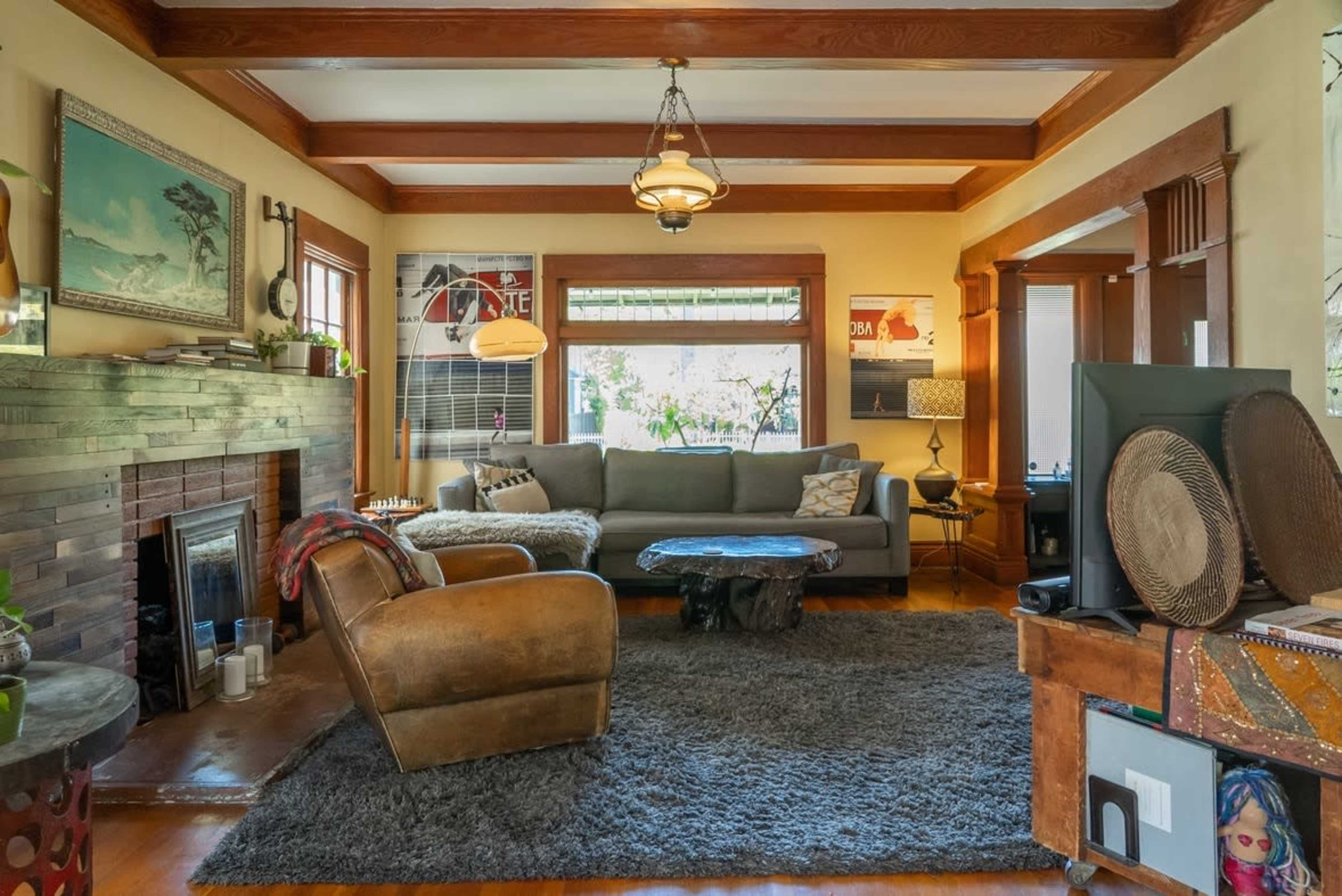 A cozy living room with a large gray sofa, a wooden coffee table, a shaggy rug, and a fireplace surrounded by wooden paneling.