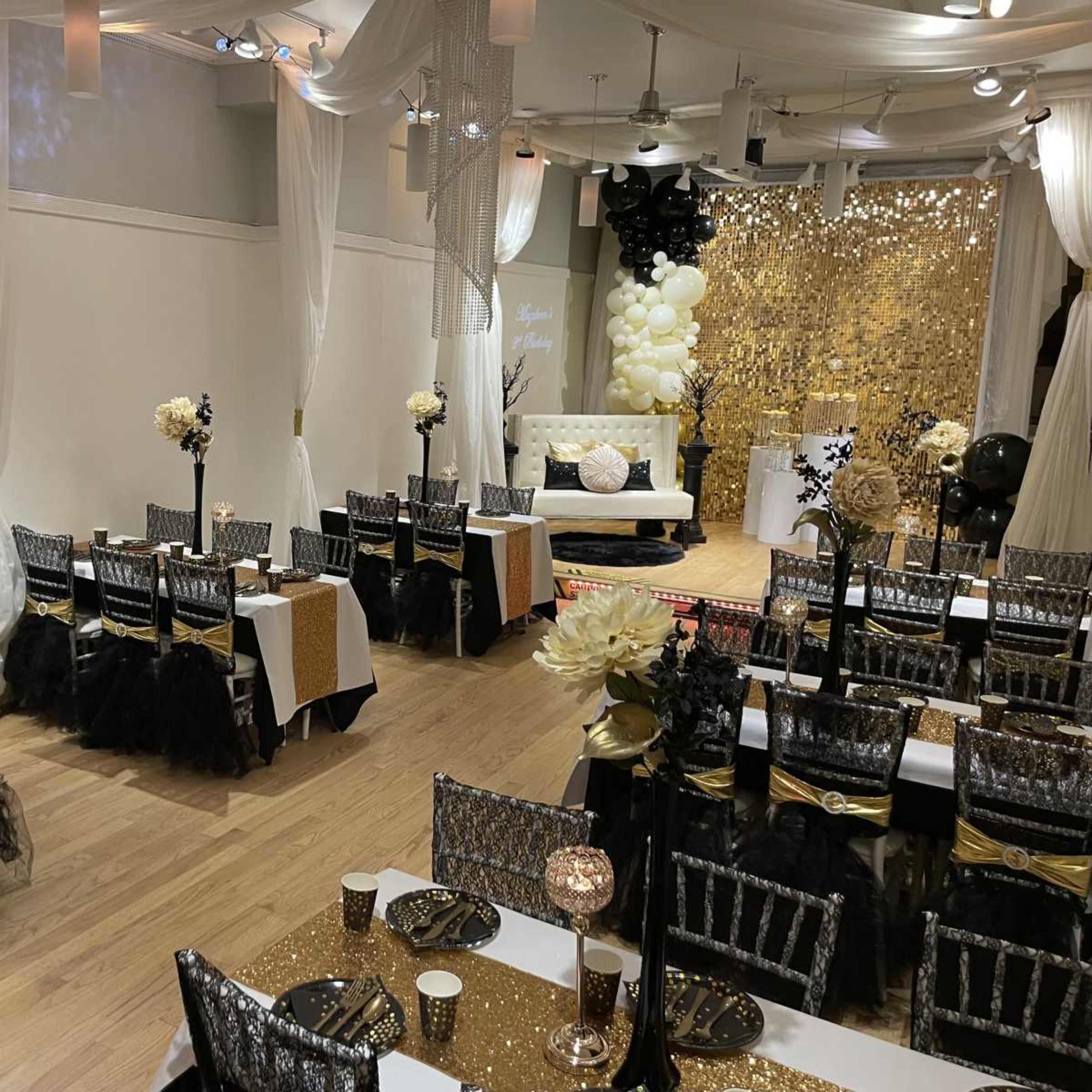 The image shows a decorated event space with tables covered in gold and black, elegant centerpieces, and a shimmering gold backdrop.