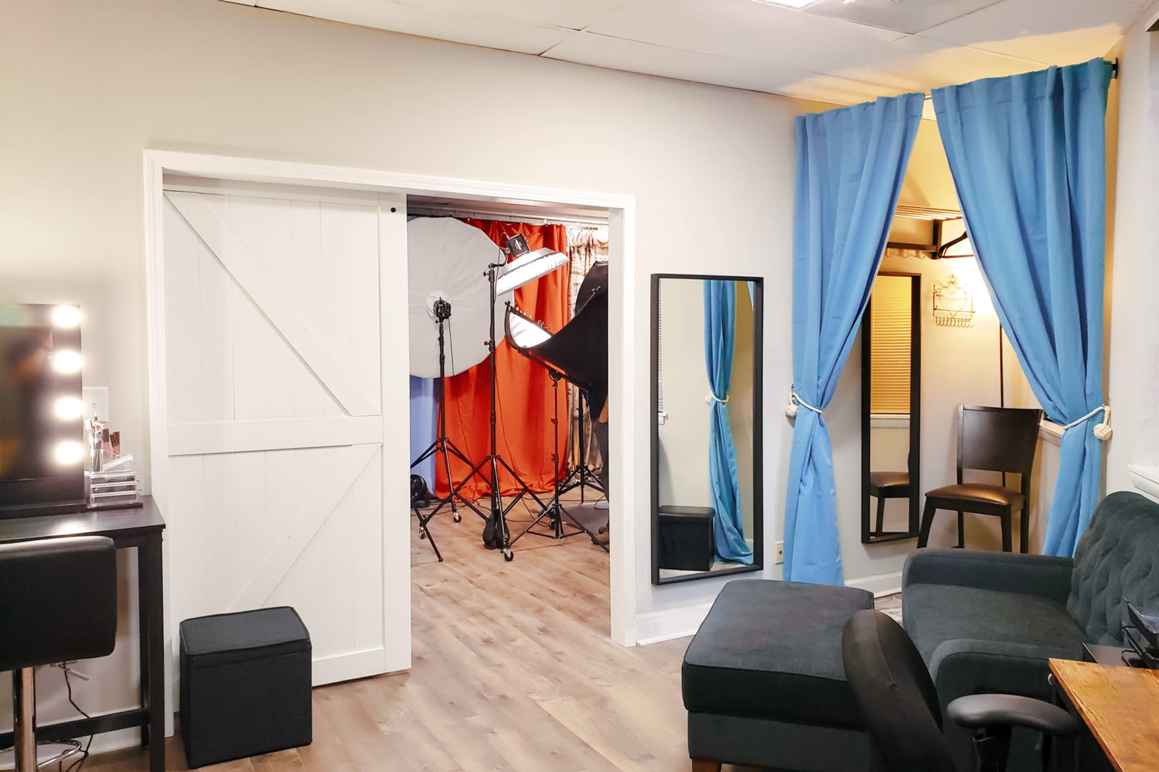 A spacious room features two curtains leading to a photo setup, with a mirror and various furniture arrangements visible.