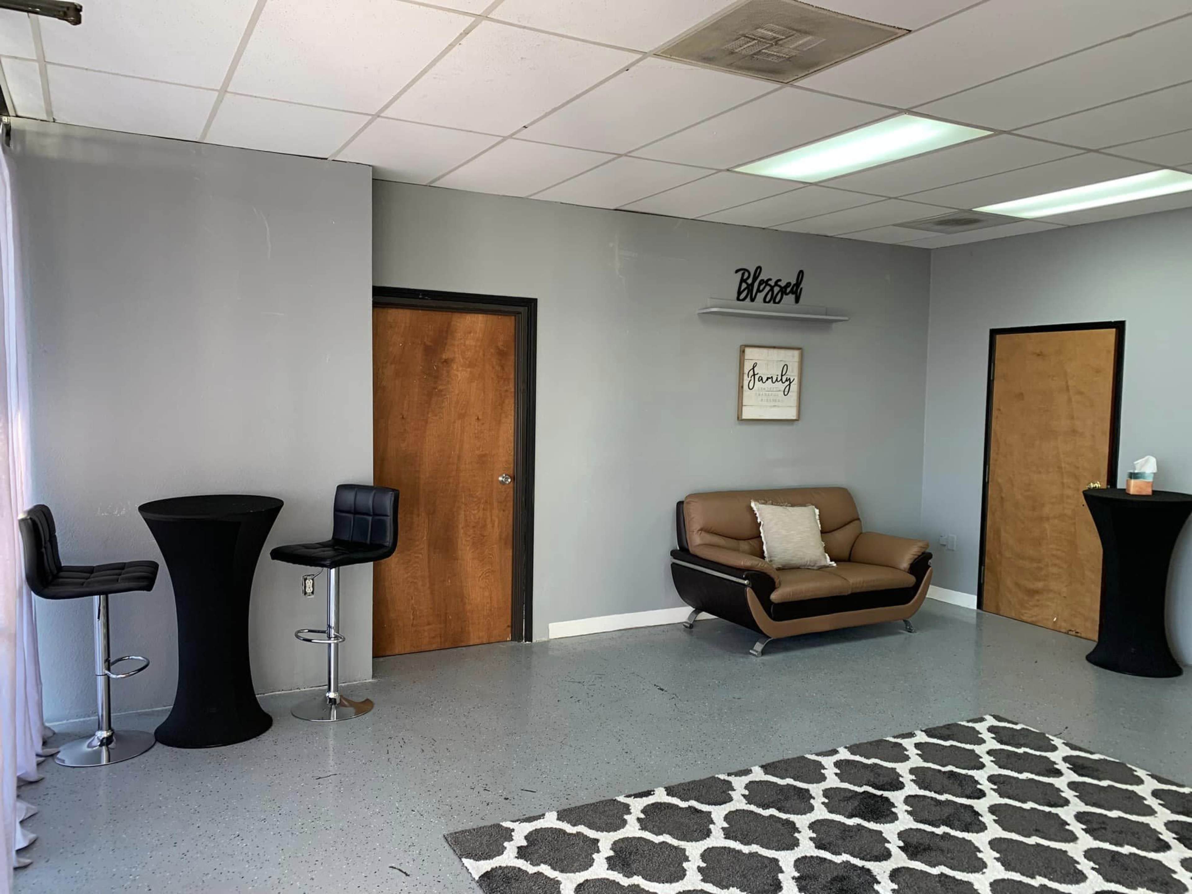 A modern interior space featuring a brown sofa, two high-top tables with stools, and decorative wall signage in muted colors.
