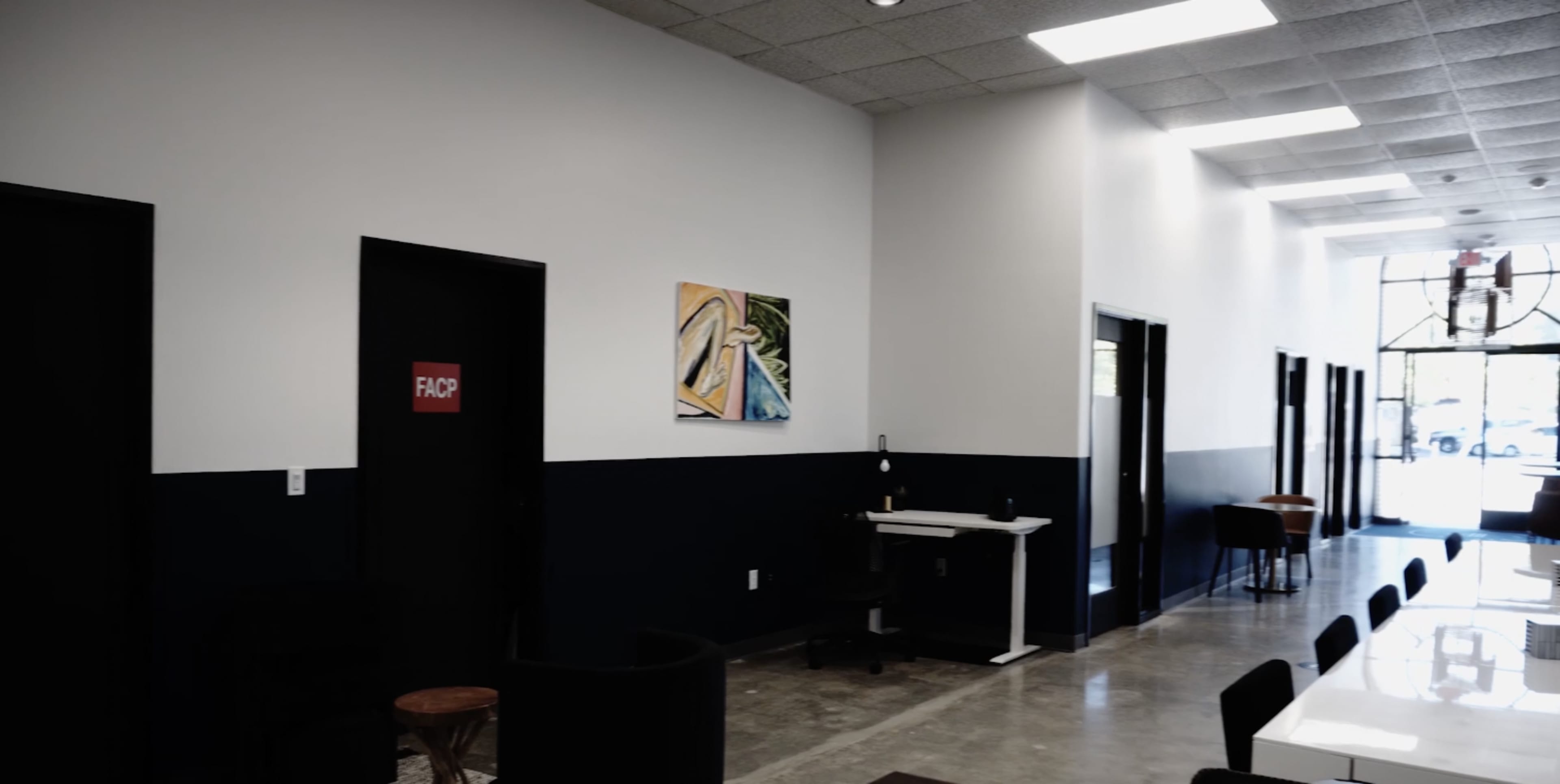 A corridor with black doors on either side, a white desk, and an artwork hanging on the wall.