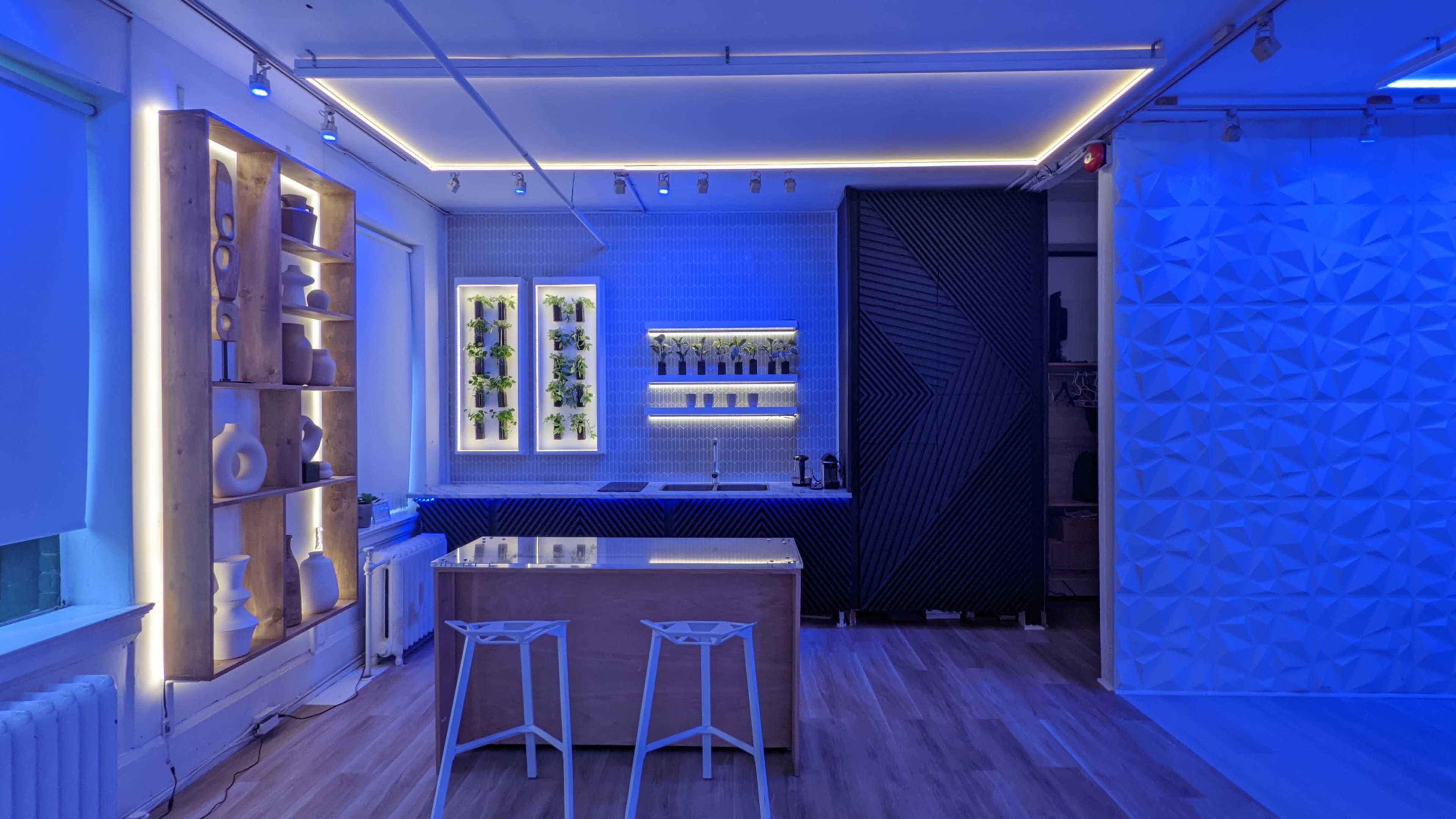 A modern kitchen space illuminated with blue lights, featuring a wooden island and a decorative wall shelf with vases.