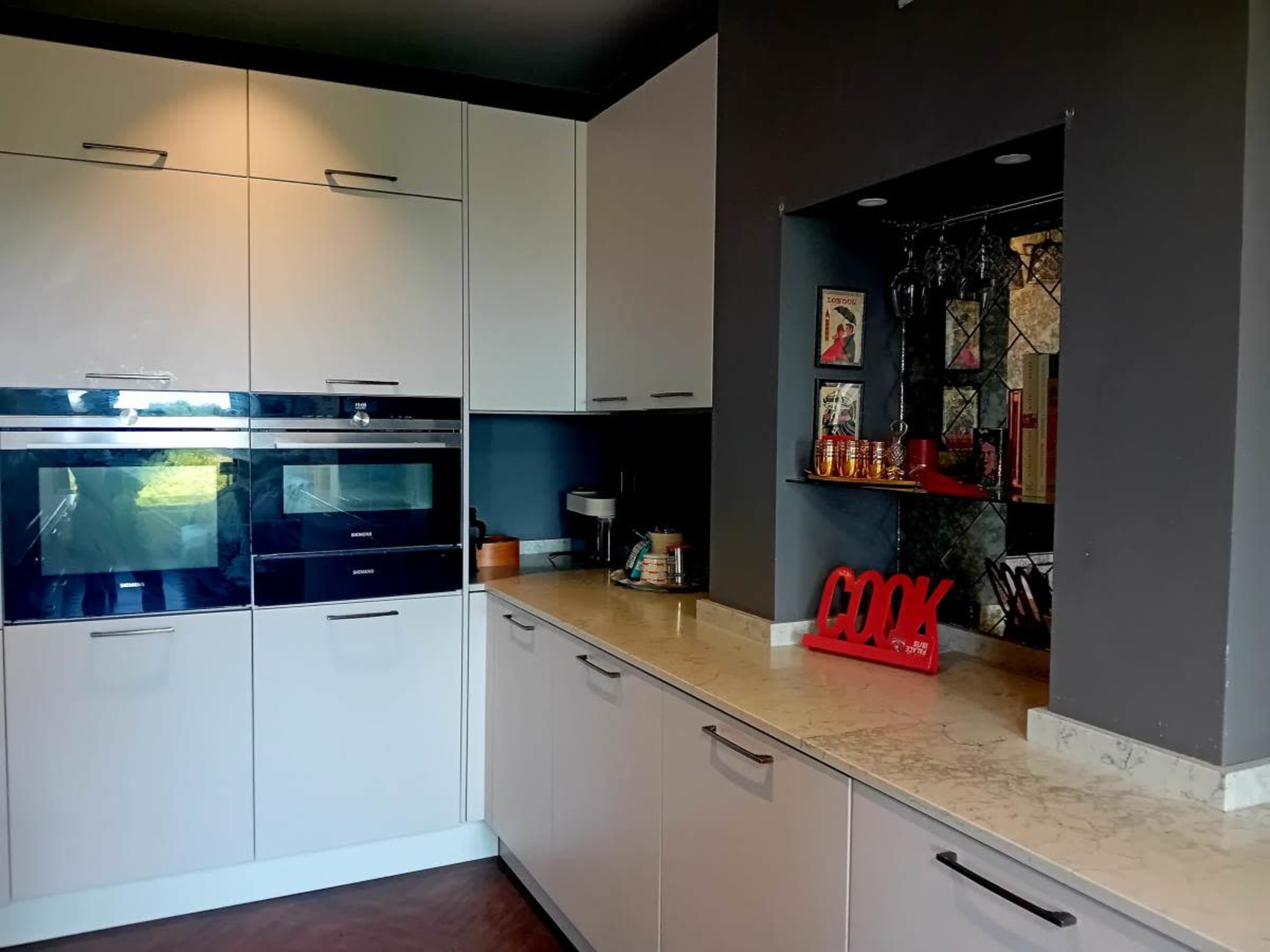 The image shows a modern kitchen with white cabinetry, built-in appliances, and a marble countertop featuring decorative items.