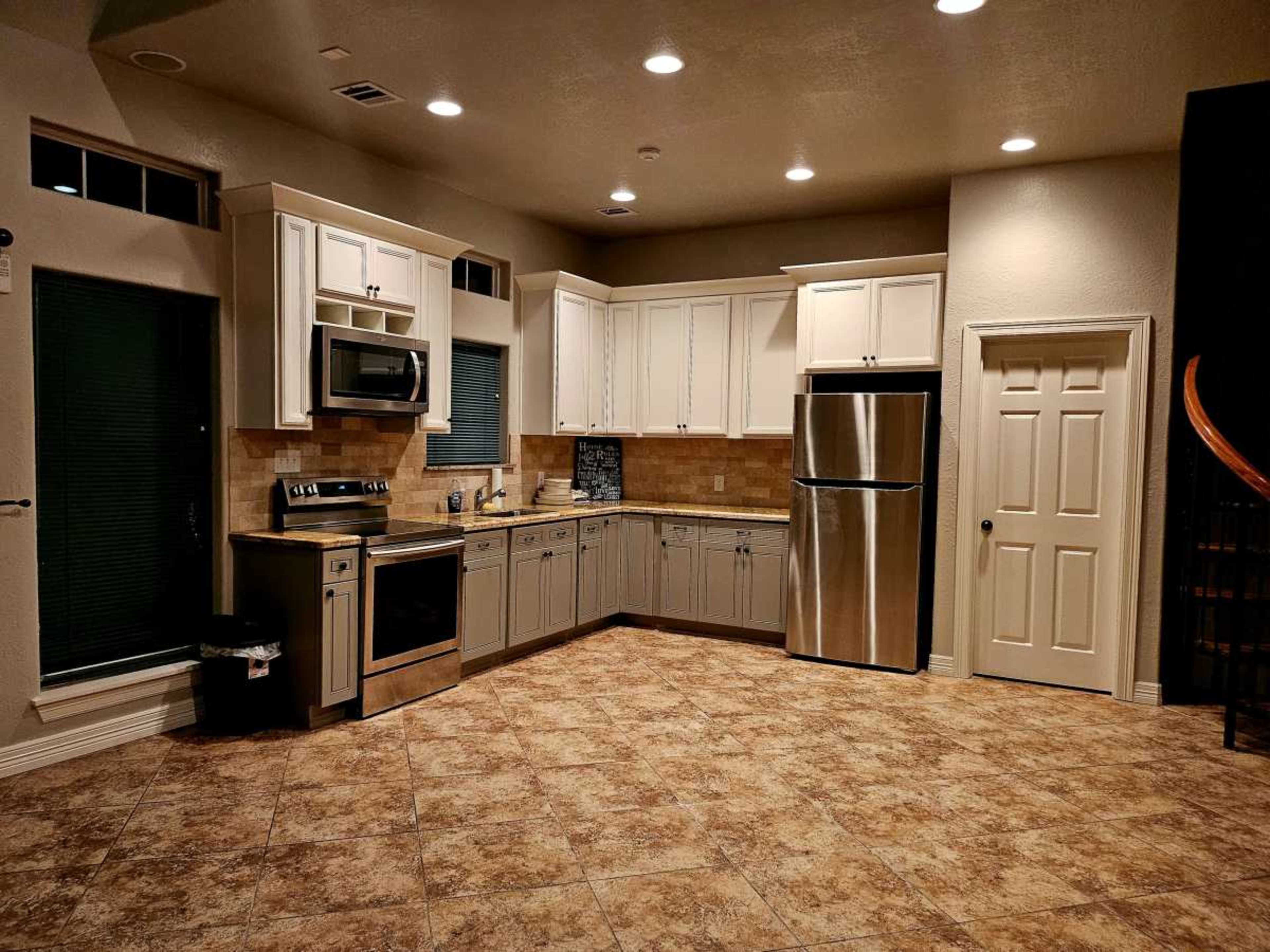 The image shows a modern kitchen with light-colored cabinets, stainless steel appliances, and a tiled floor.