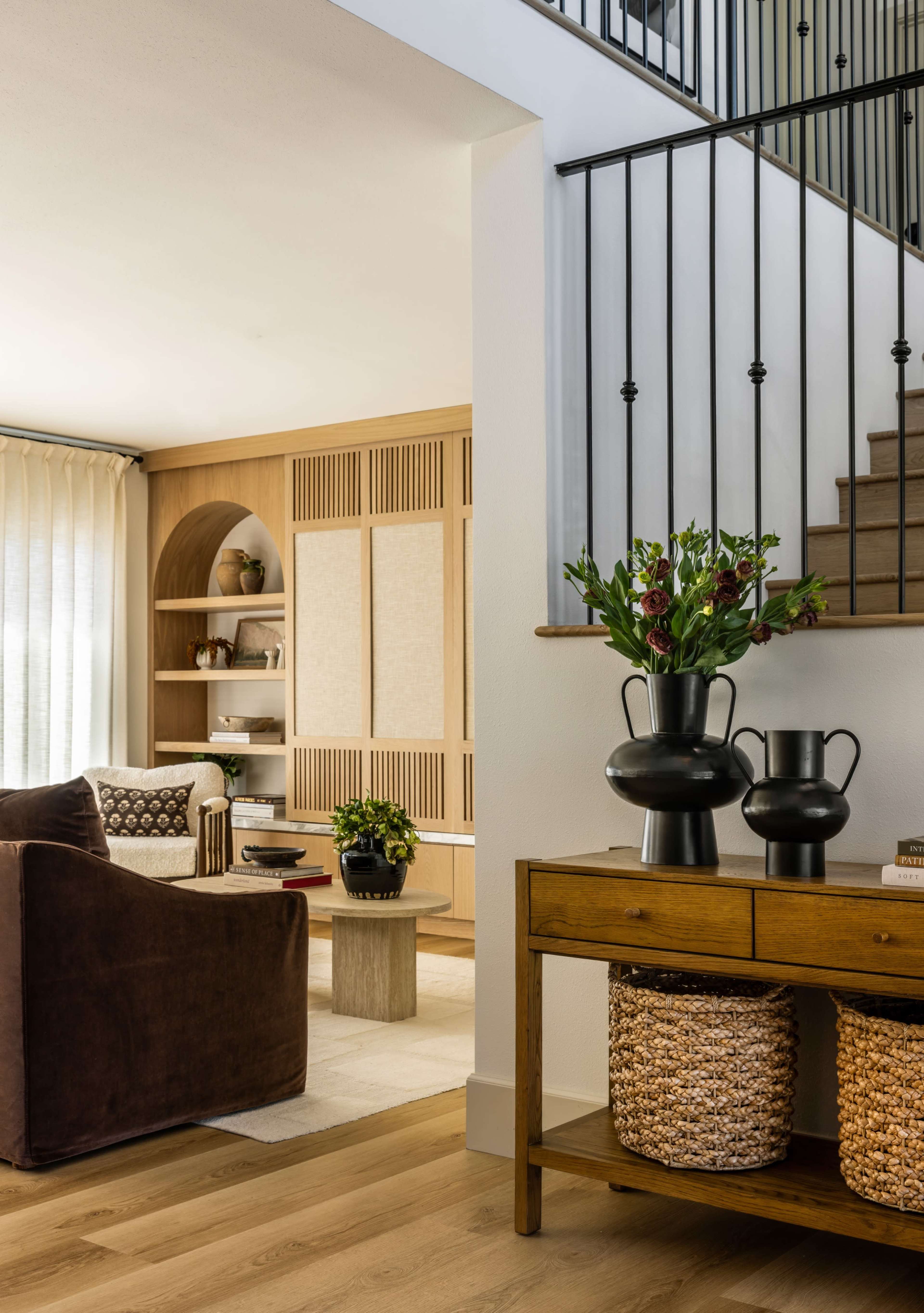 The image shows a modern living area featuring a staircase, a wooden console table with decorative vases, and a cozy seating arrangement.
