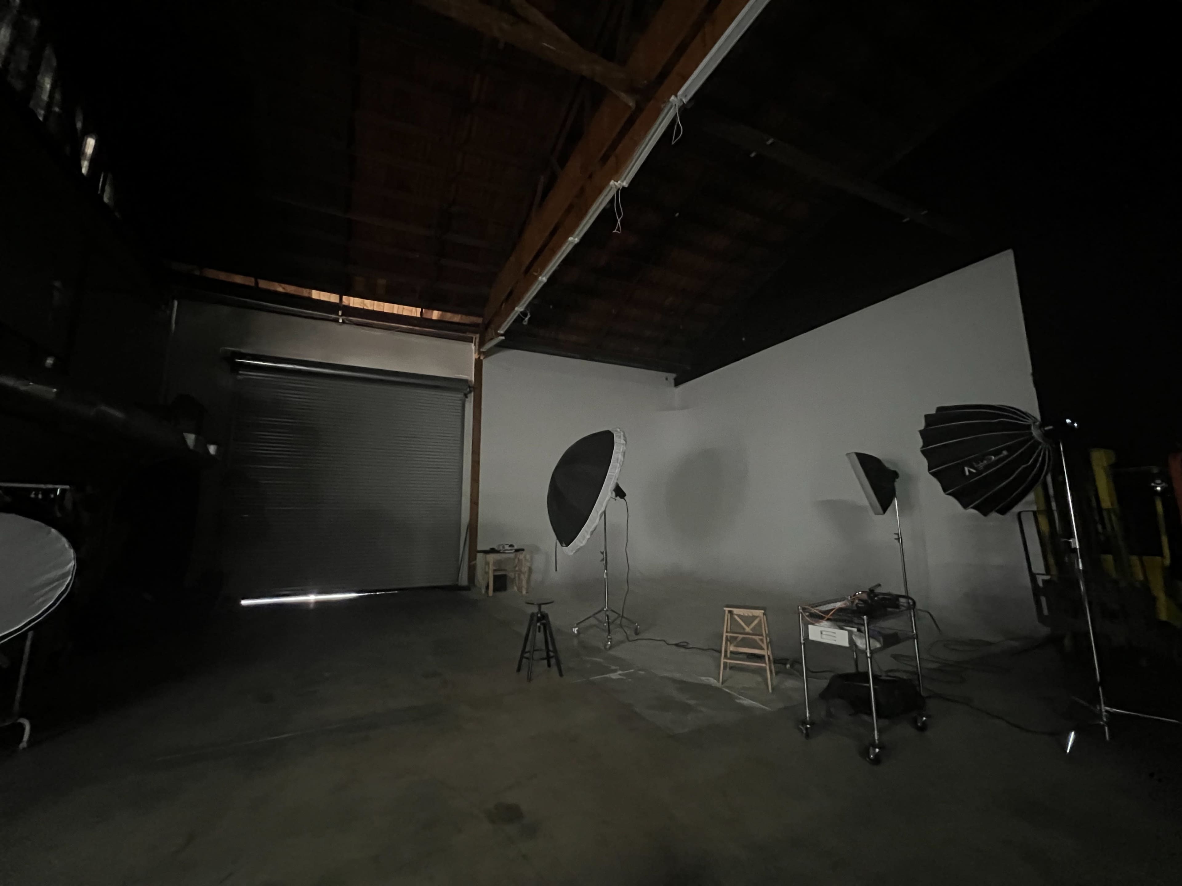 A dimly lit photography studio features various lighting equipment arranged near a blank white wall.