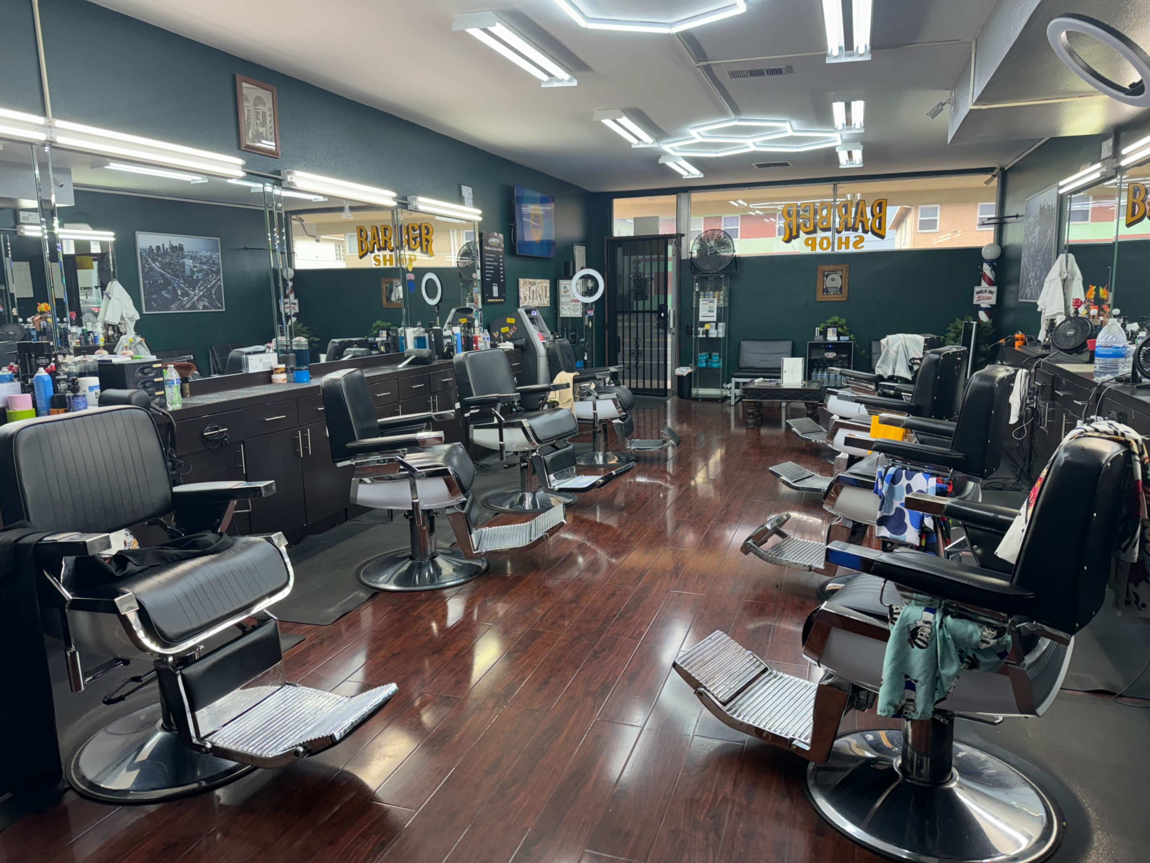The image shows an empty barbershop featuring several black barber chairs arranged around a central area with mirrors and styling tools visible on countertops.