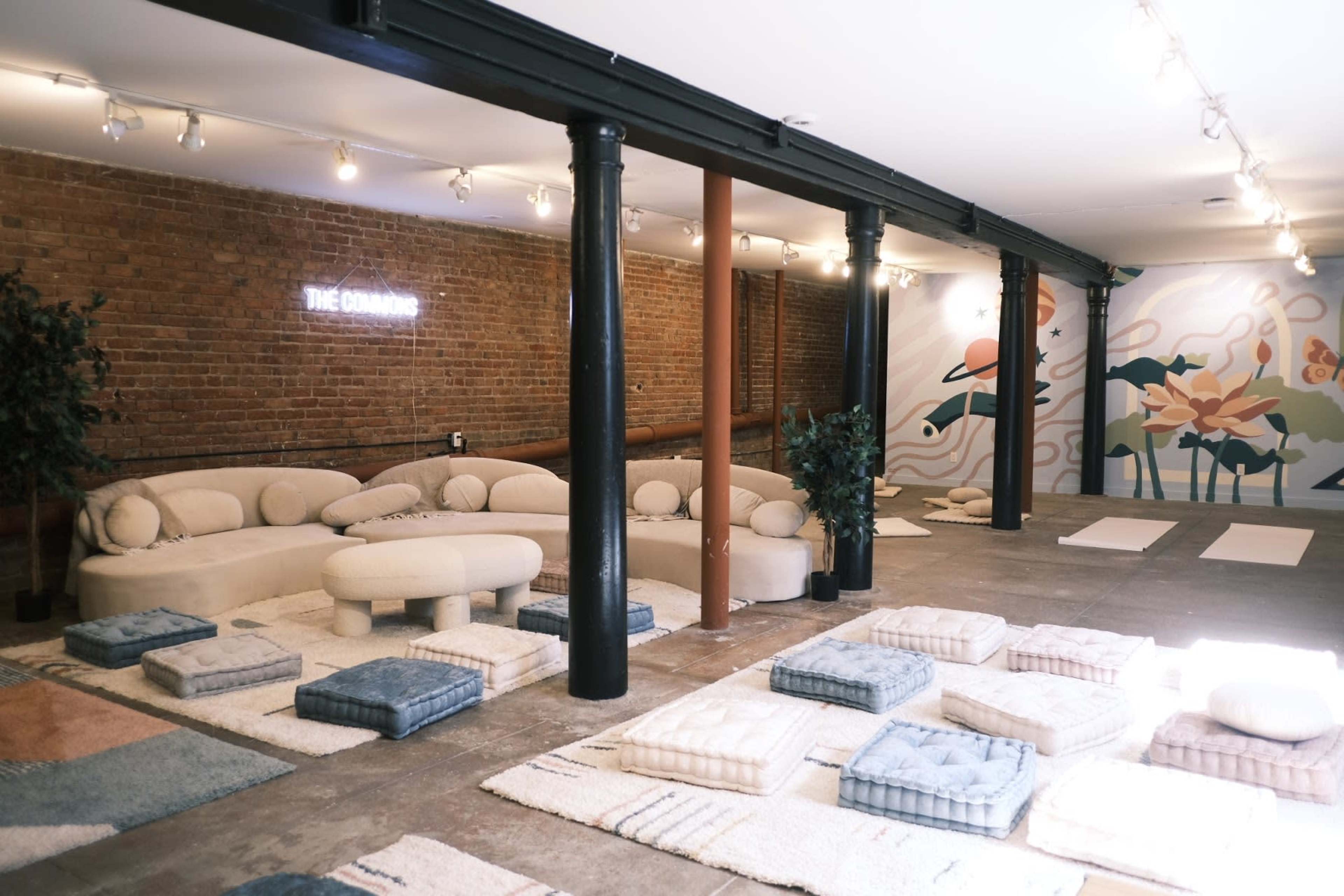 A spacious room with a textured brick wall, featuring soft seating arrangements and cushioned mats on a concrete floor.
