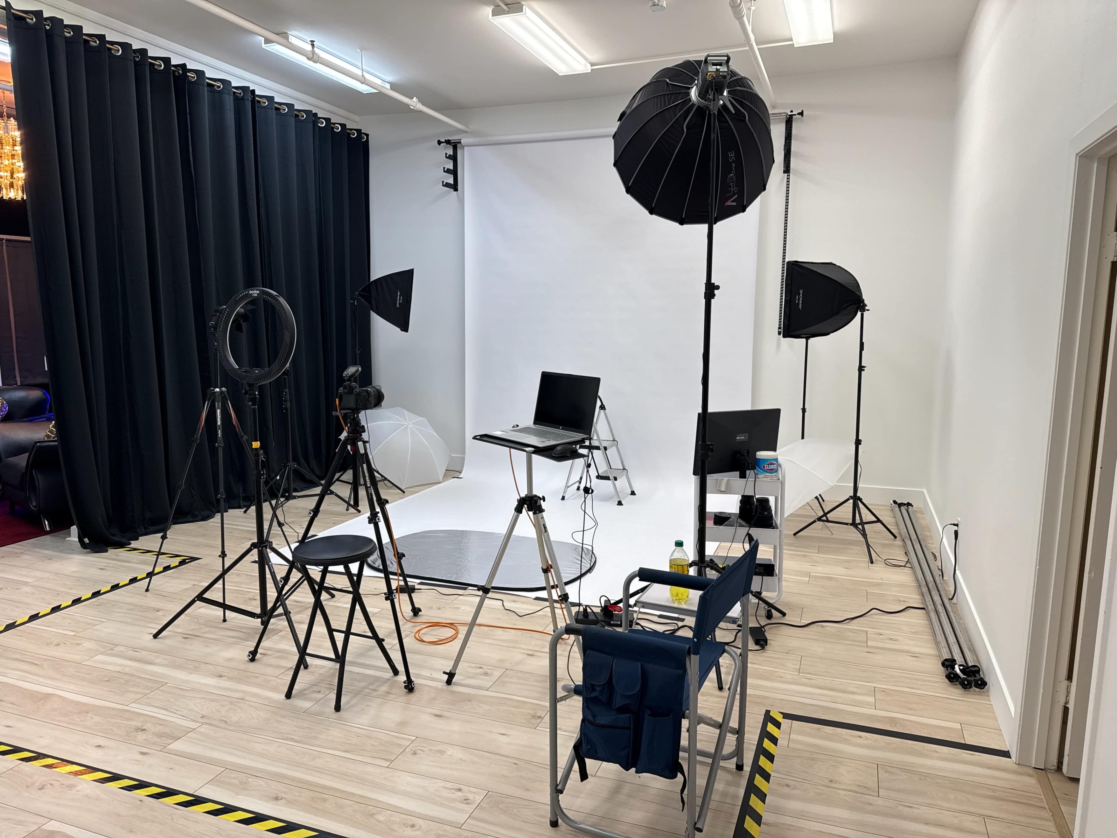 The image shows a photography studio setup with multiple lighting equipment, tripods, a backdrop, and seating arranged for a photoshoot.