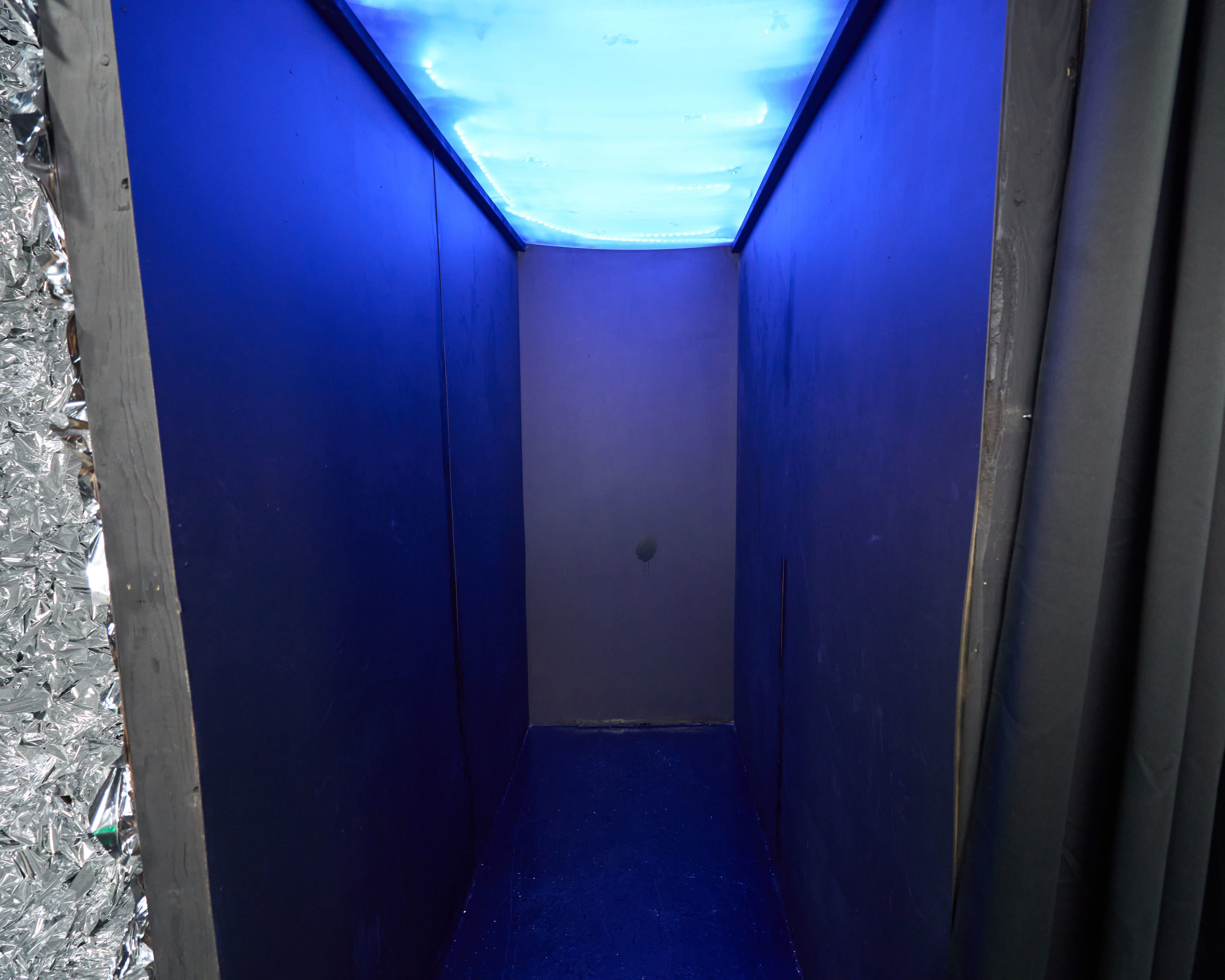 The image shows a narrow corridor with dark walls and a glowing blue ceiling.