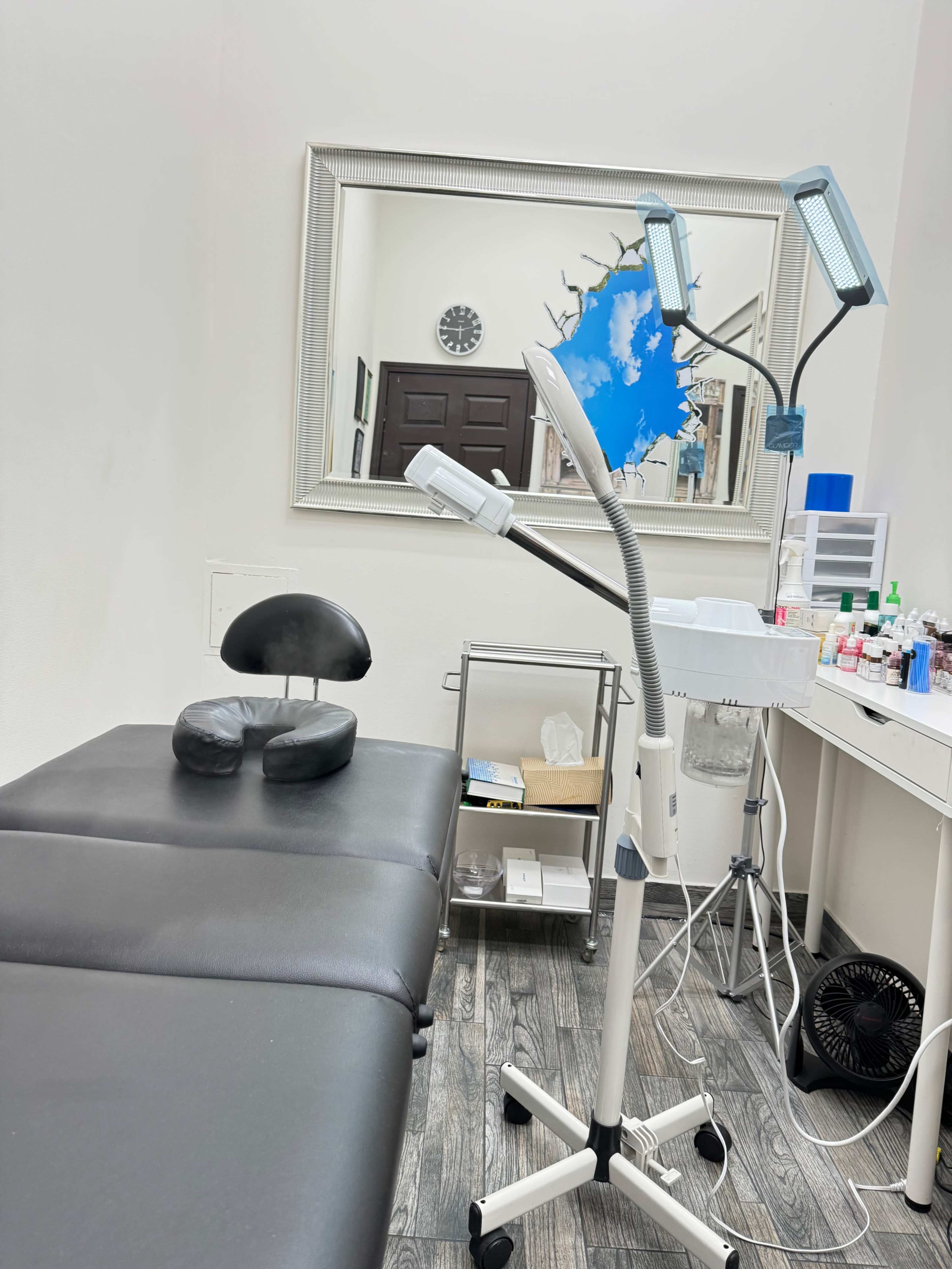 The image shows a treatment room with a black massage table, a large mirror reflecting a wall clock, and various medical equipment organized on a nearby counter.