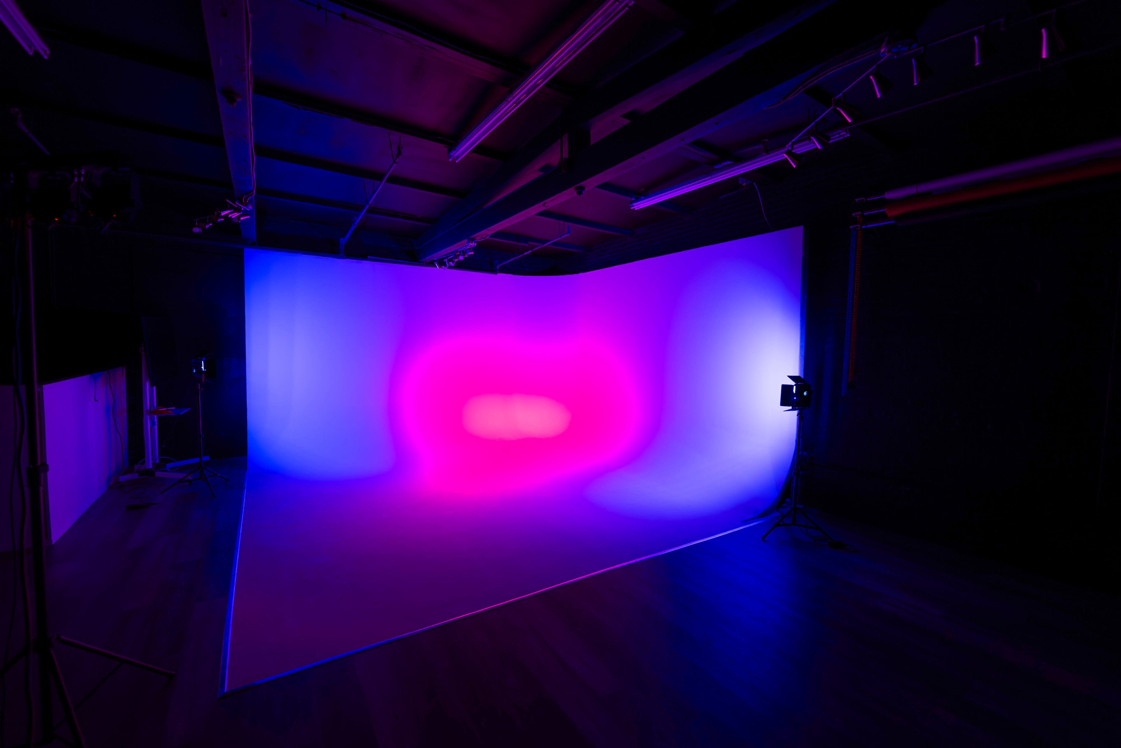 A photography studio features a gradient backdrop illuminated by vibrant purple and blue lights.
