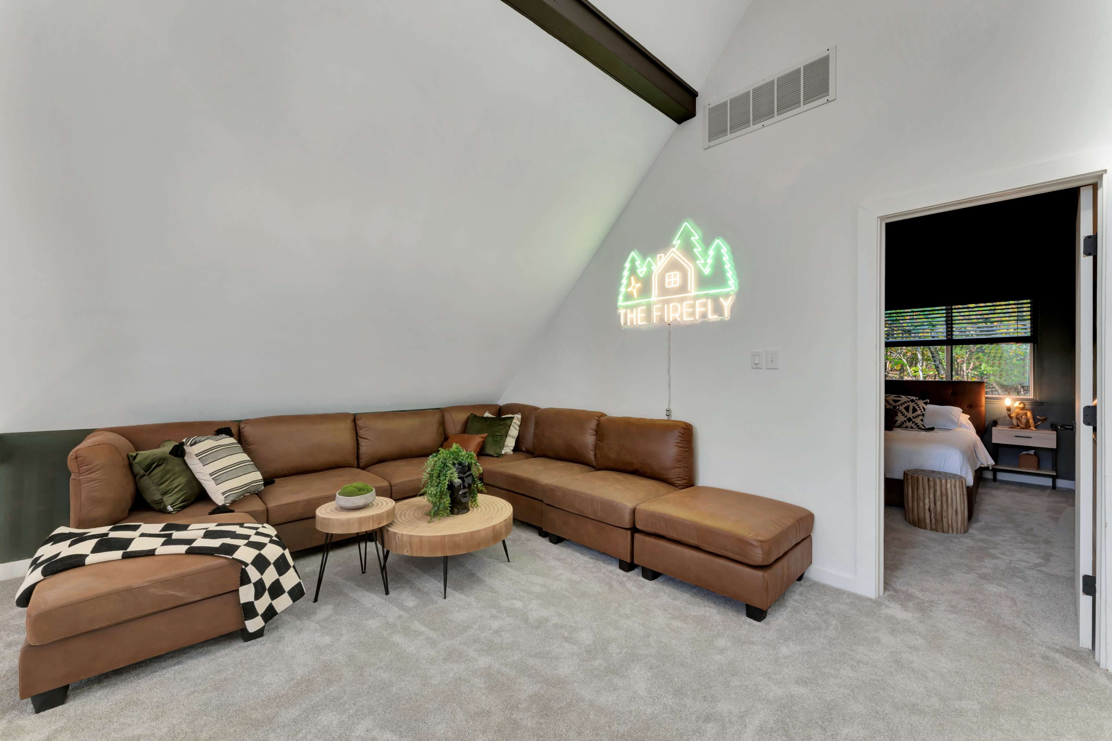 A cozy living area features a brown sectional sofa, a wooden coffee table, and a neon sign that reads "The Firefly" on a white wall.