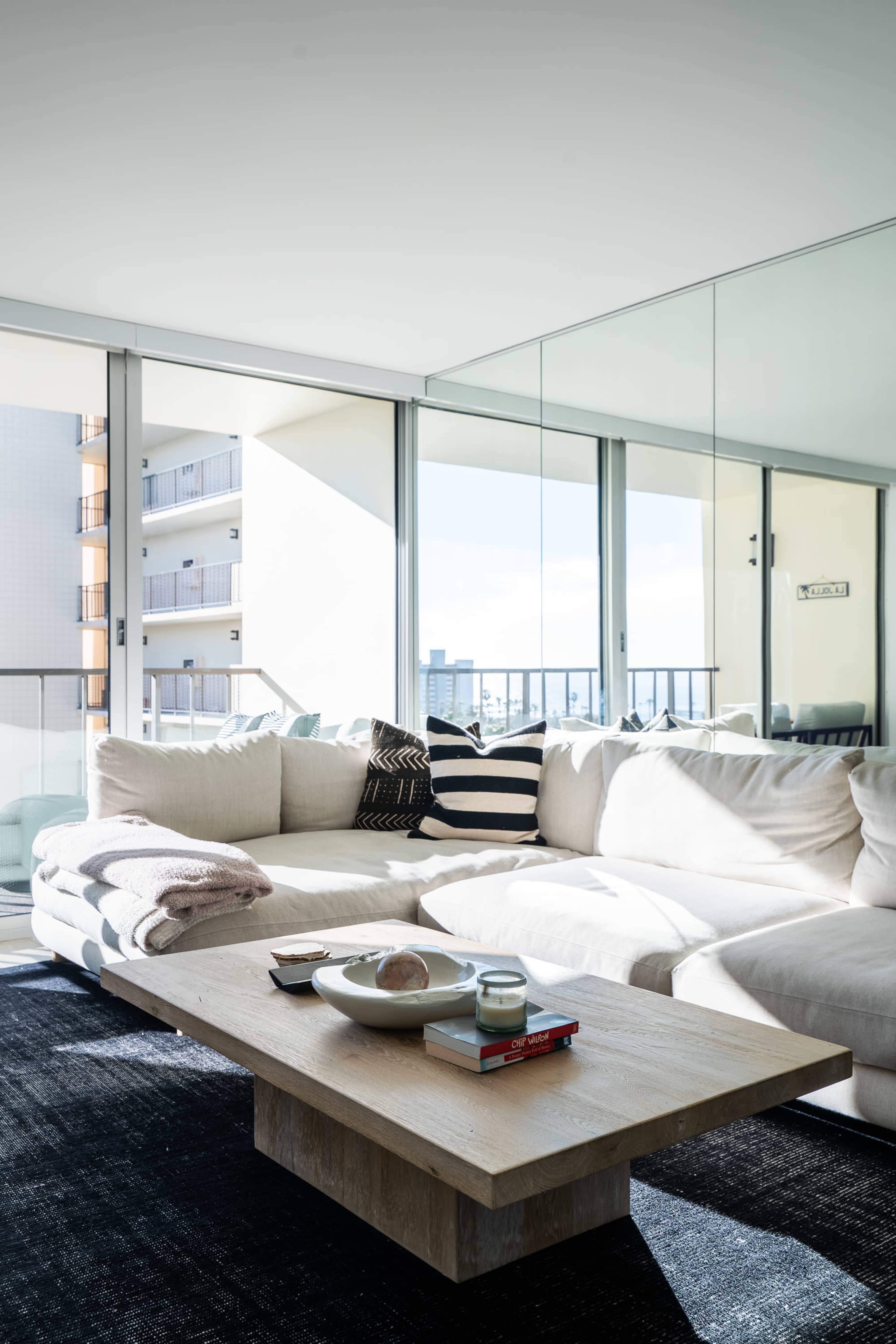 A spacious, modern living room features a large sectional sofa, a wooden coffee table with décor items, and expansive windows letting in natural light.