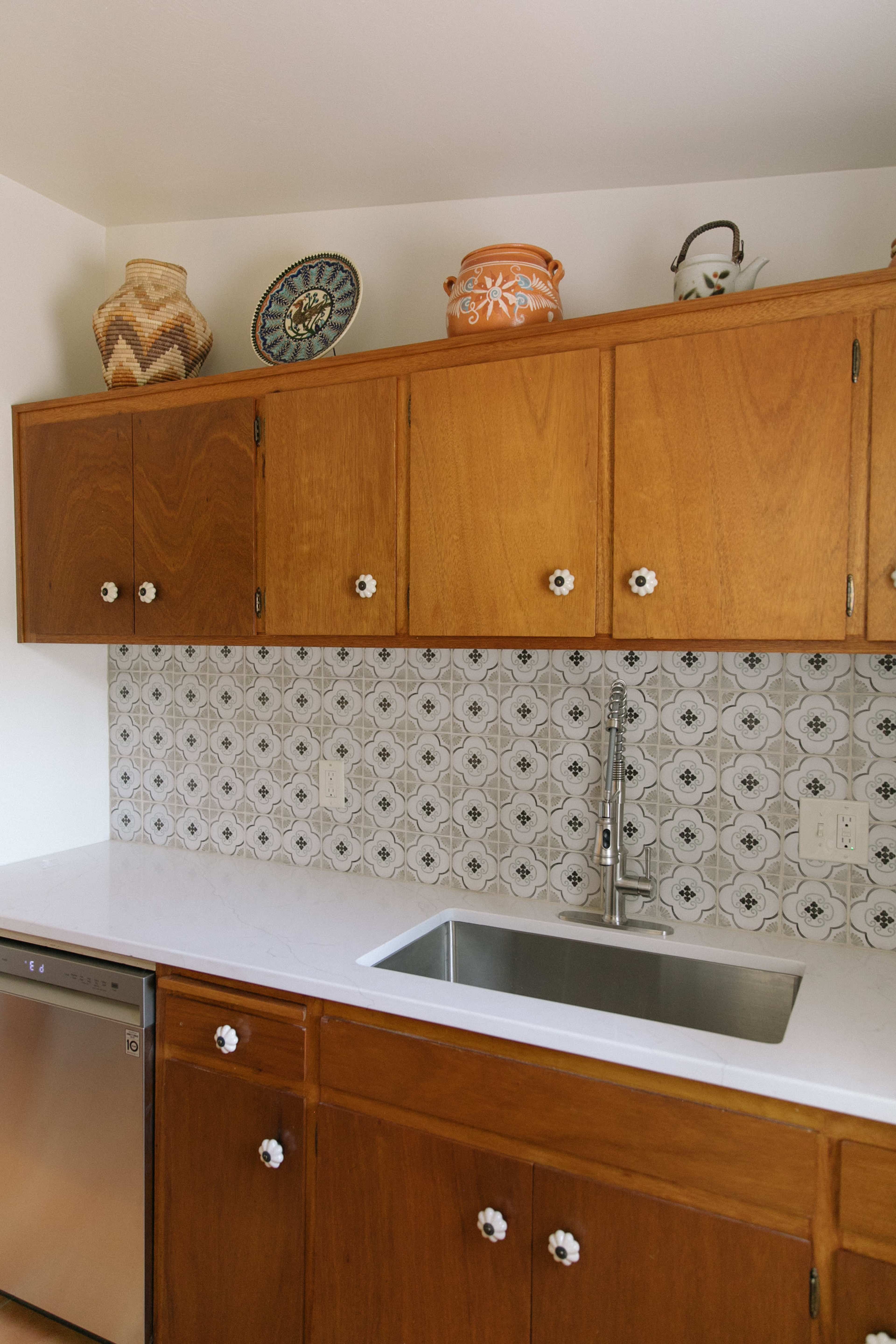 The kitchen features wooden cabinets with ceramic handles, a stainless steel sink, and decorative pottery on the shelves above a tiled backsplash.