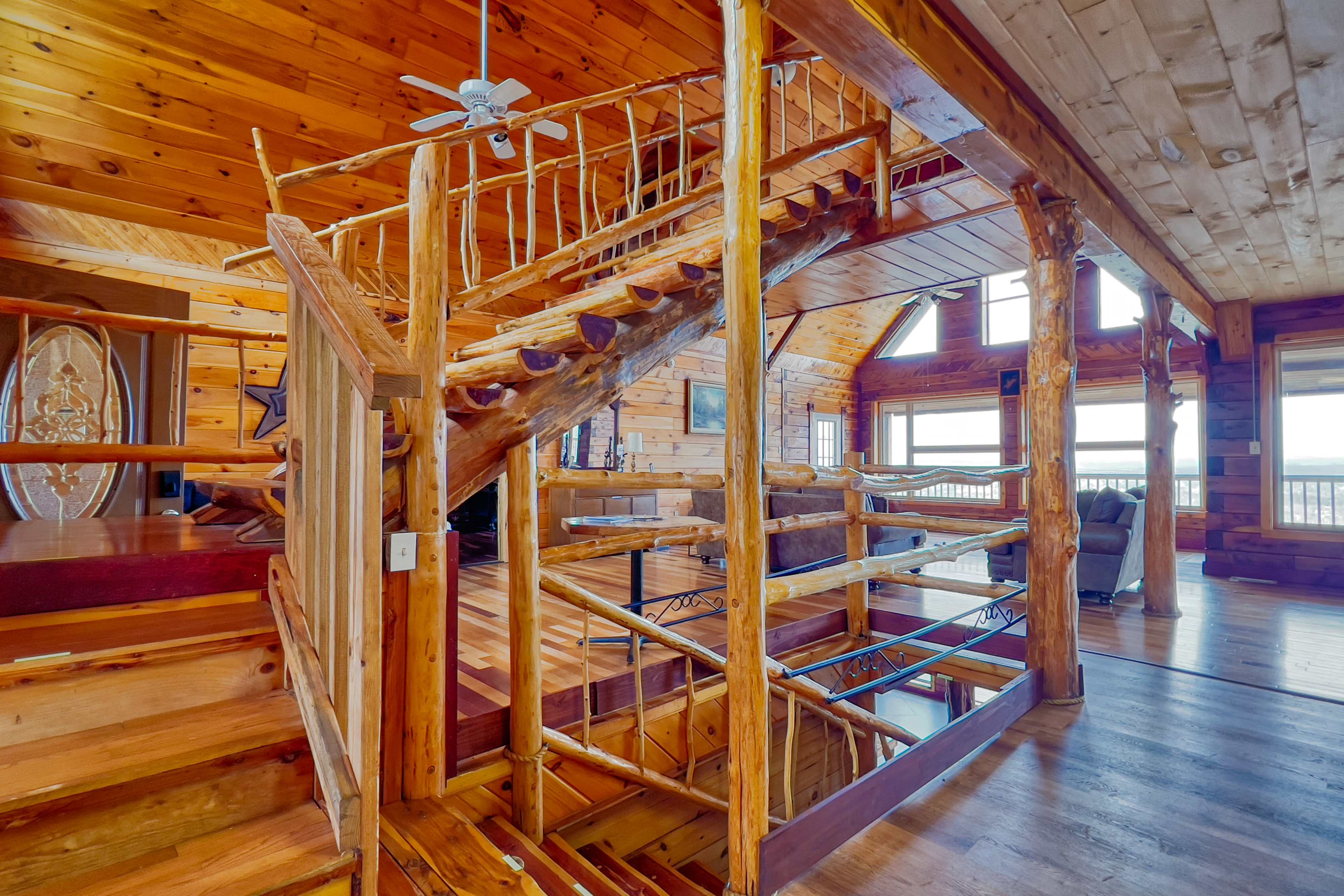 A wooden staircase with a curved design in a log cabin interior, featuring large windows that provide natural light and a view of the outdoors.