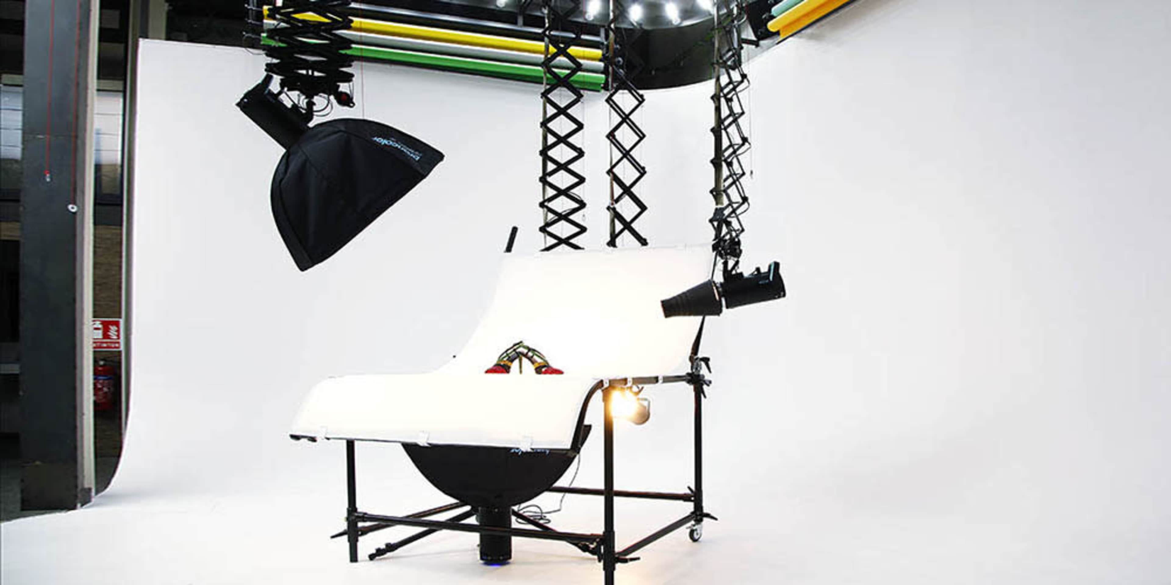 A photography setup with white backdrop, lighting equipment, and a raised platform on a wheeled frame.