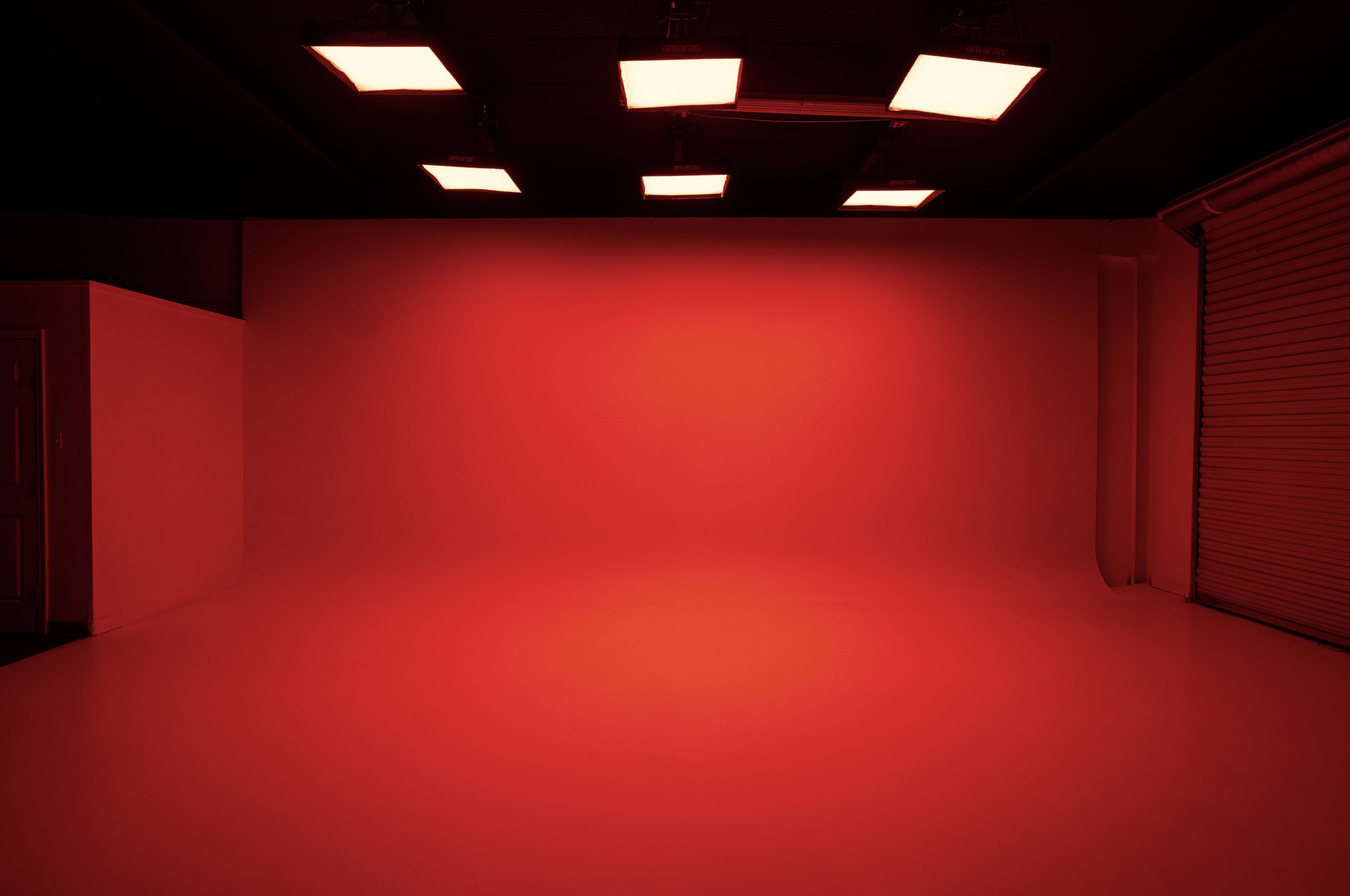 The image shows a red-lit studio space with a smooth floor and a wall featuring overhead square lights.