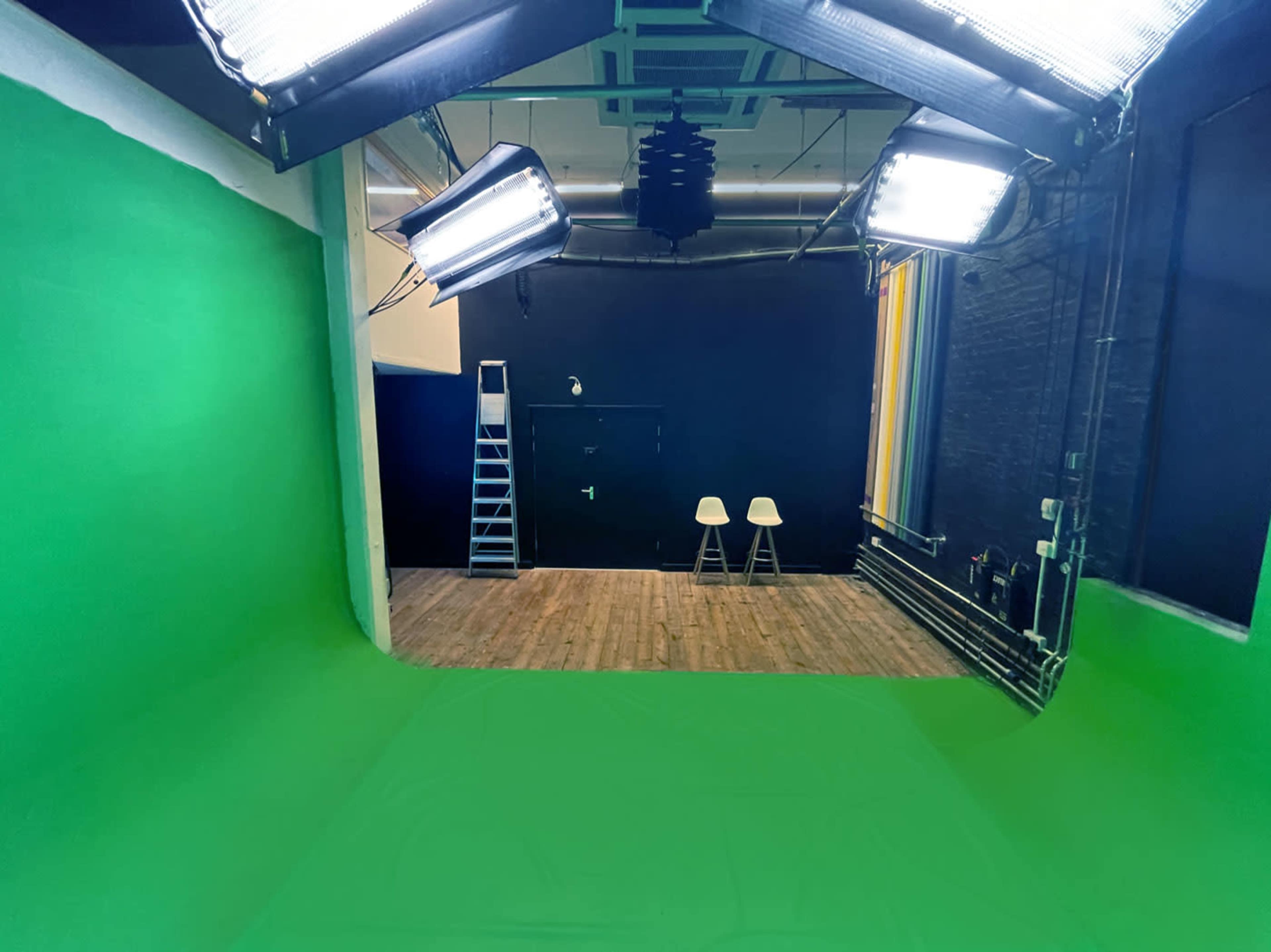 A green screen studio with two white chairs, a ladder, and overhead lighting fixtures.