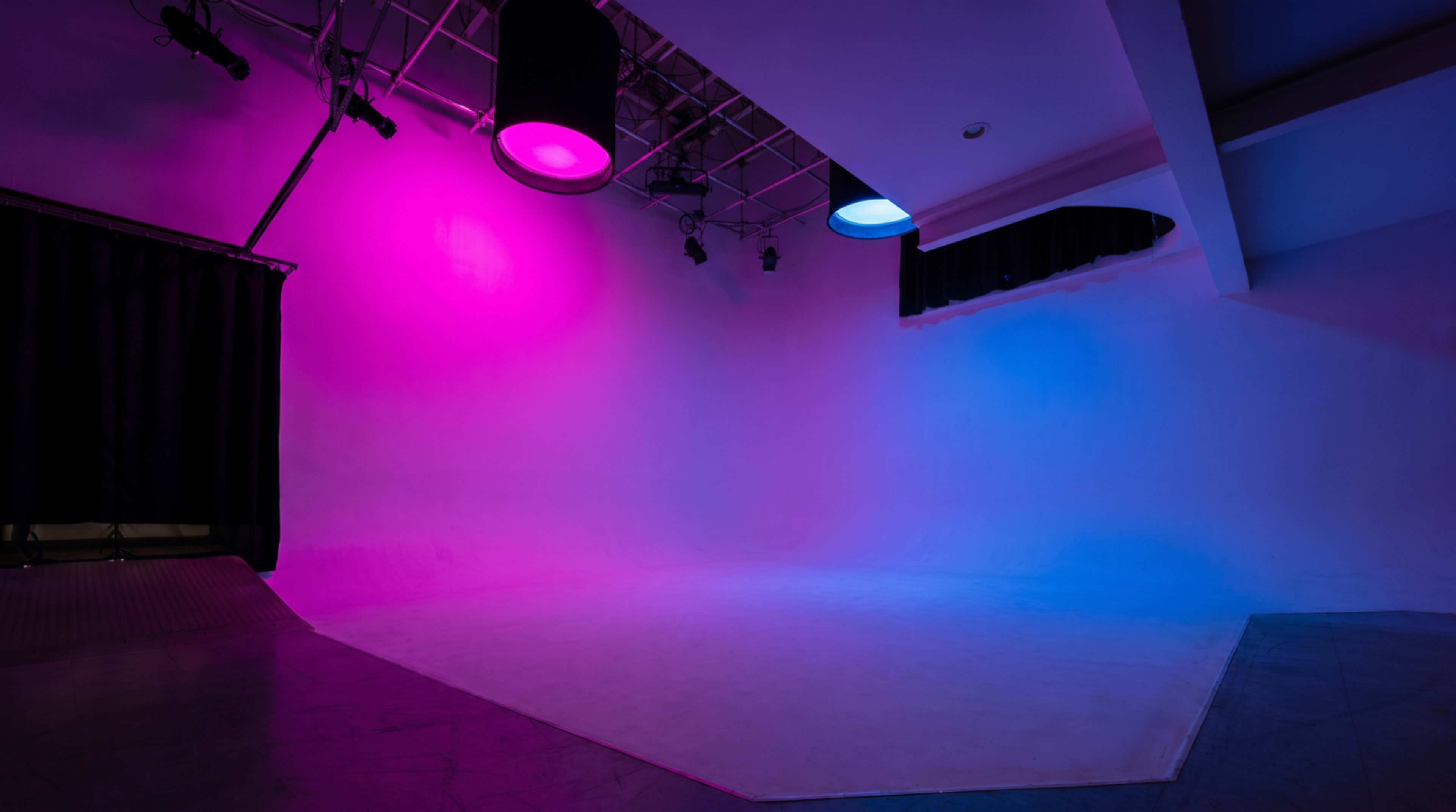 The image shows a photography studio with a gradient backdrop illuminated by pink and blue lights.