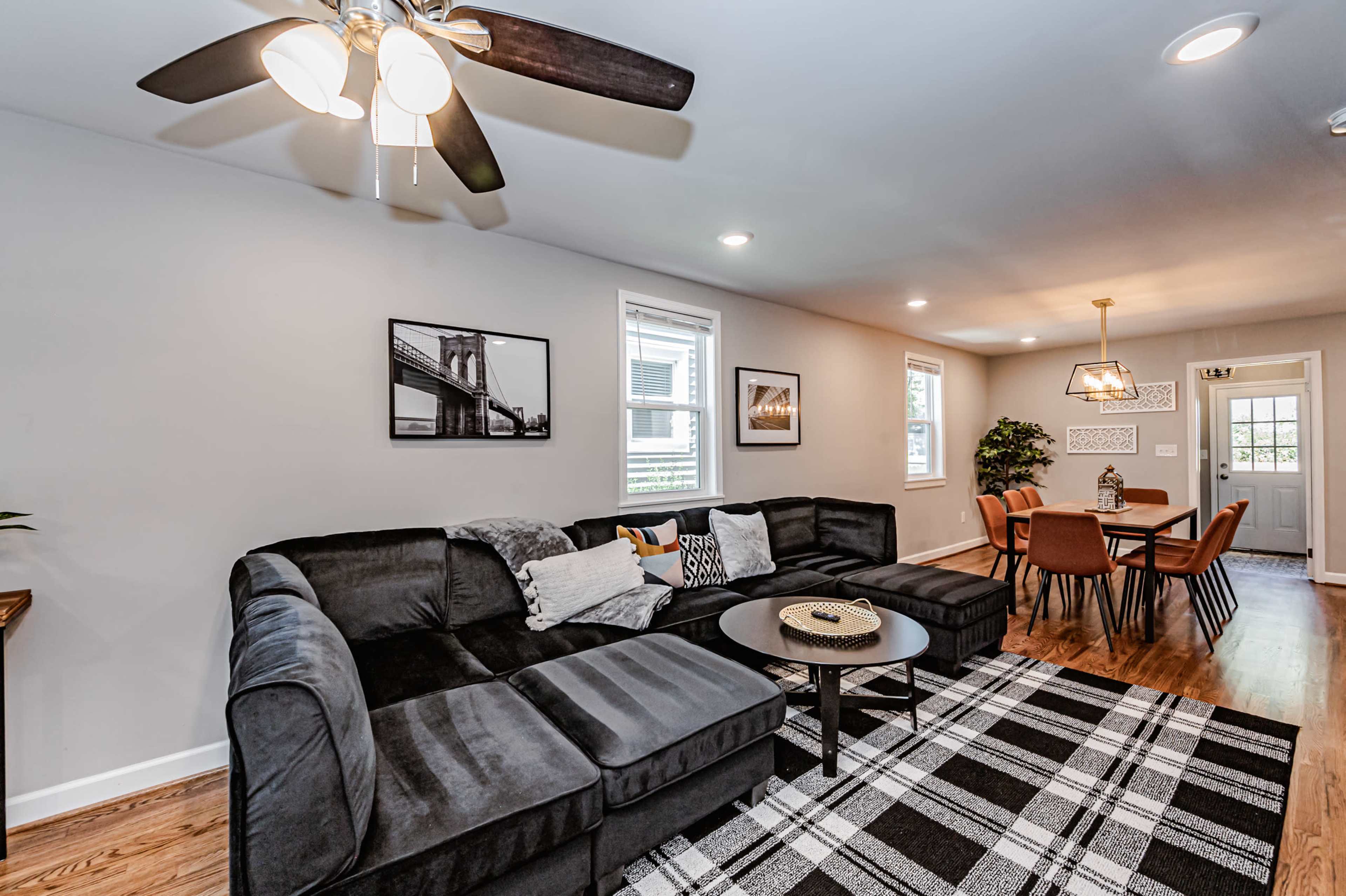 A modern living room with a sectional sofa, a round coffee table, and a dining area featuring a table and chairs, all illuminated by natural light and ceiling fans.
