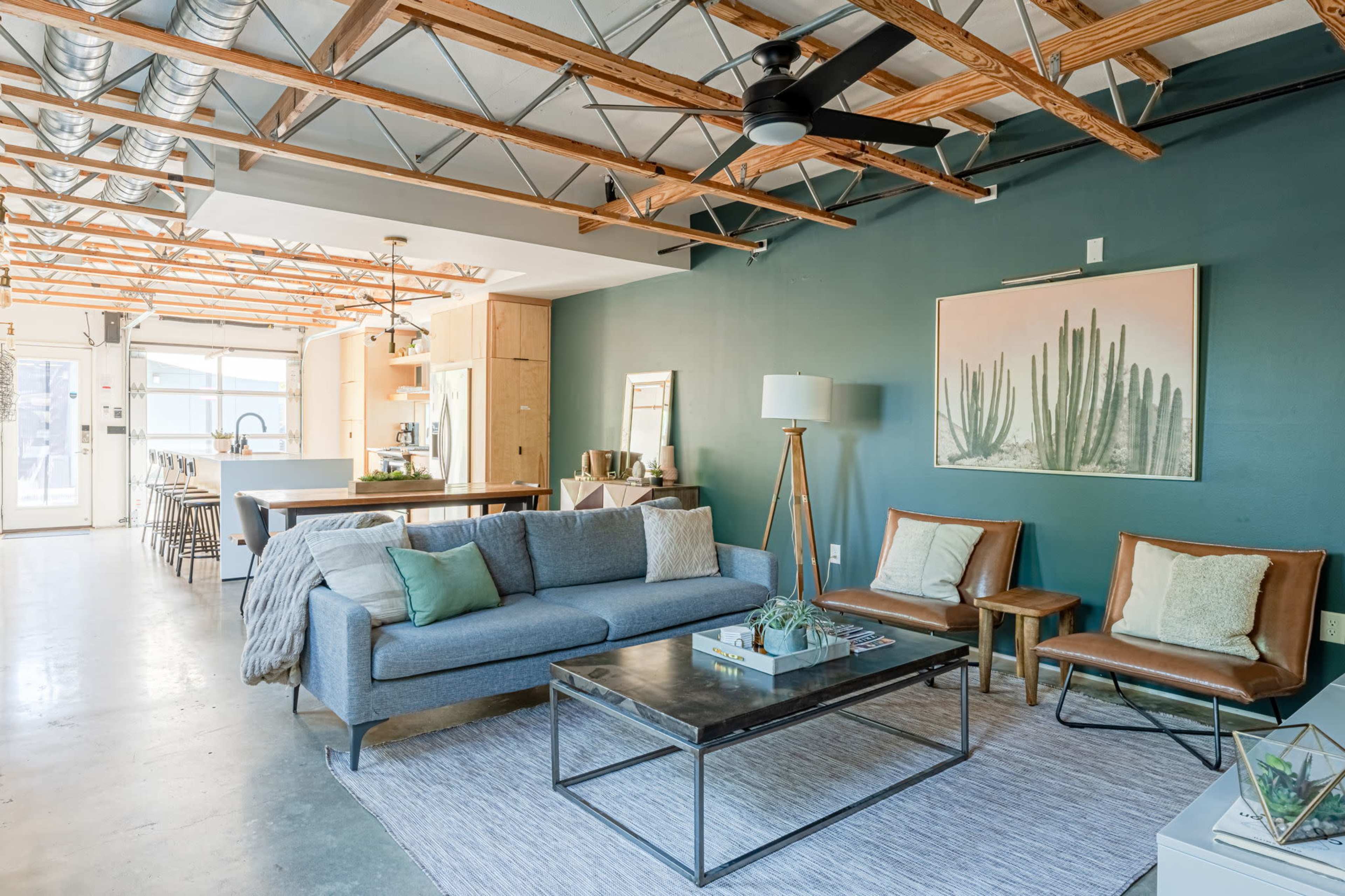The image shows a modern living space with a gray sofa, leather chairs, a metal coffee table, and a large piece of artwork on a green wall.