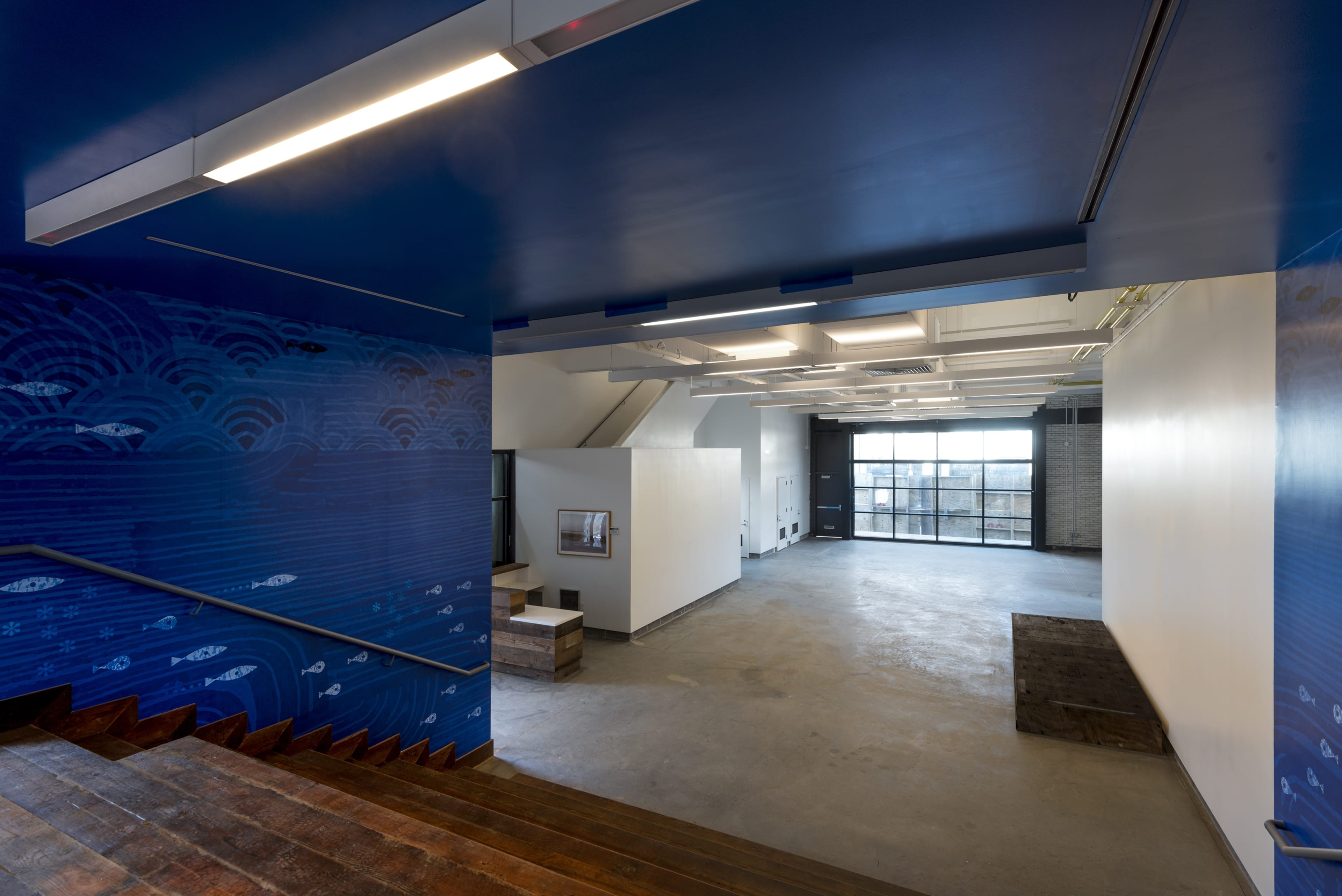 A spacious, modern interior with blue and white walls, large windows, and a staircase leading down to an open area.