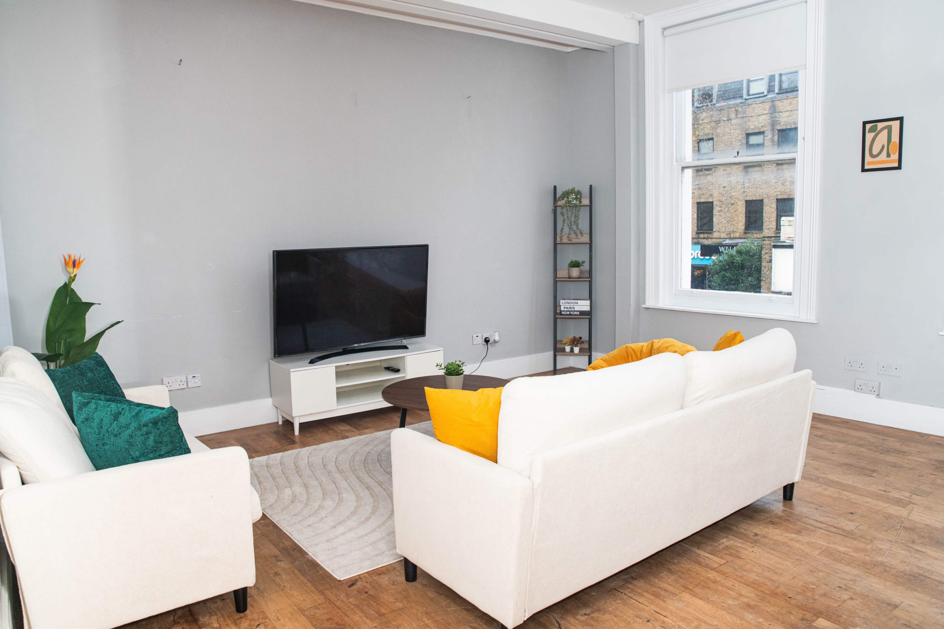A cozy living room features two sofas, a coffee table, and a television, with natural light coming through a large window.