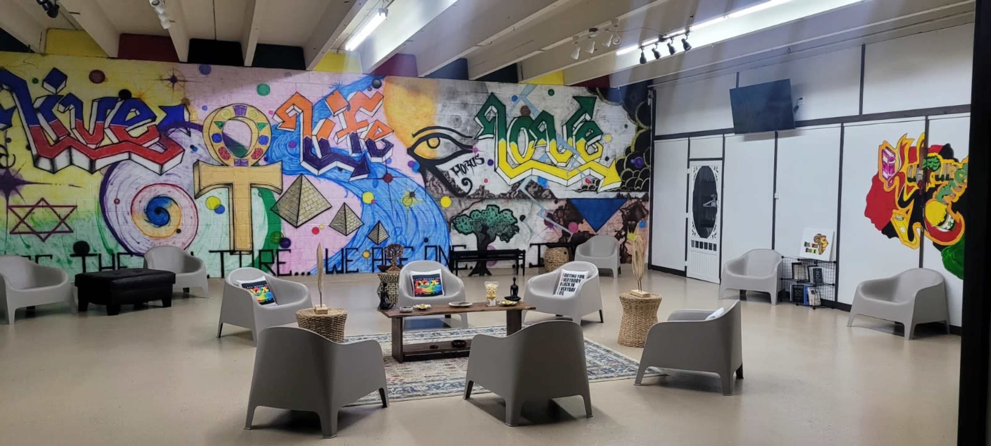 A brightly colored room featuring a large mural on the wall and several seating arrangements with modern chairs and a low table in the center.