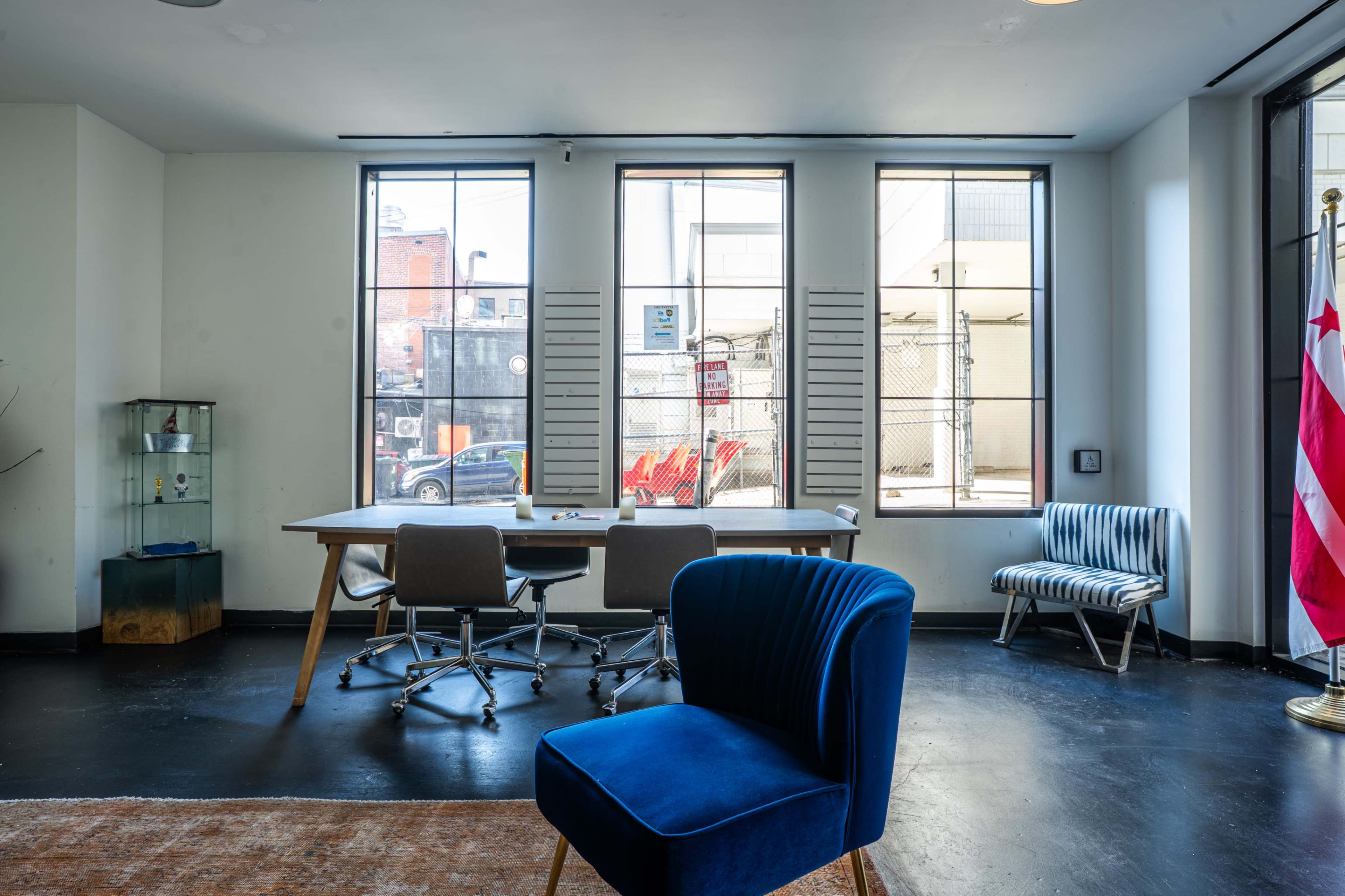 A modern office space features a large wooden table surrounded by chairs, with large windows that overlook an outside area.