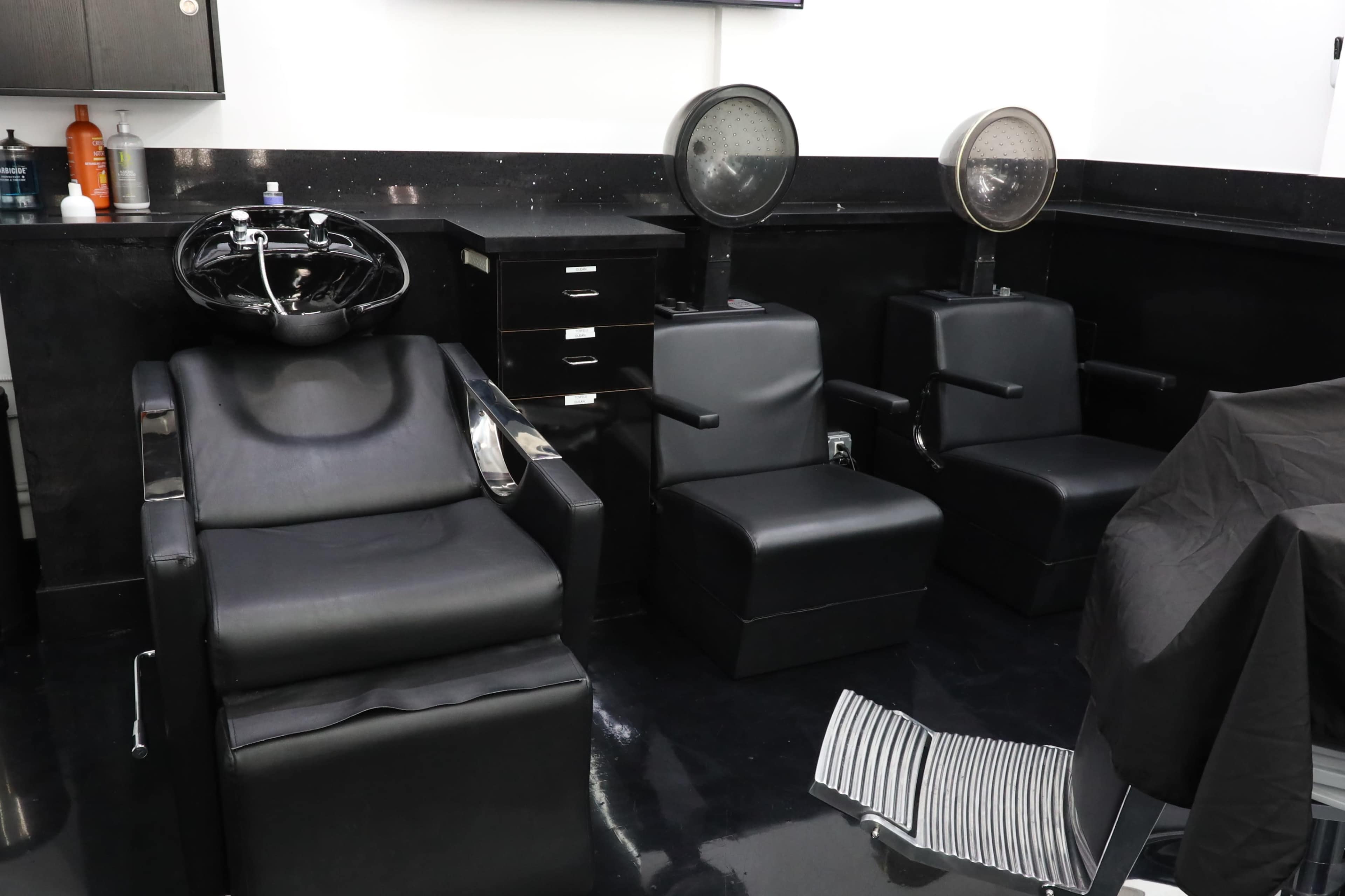 A modern hair salon with two black chairs for client services and a styling station in the background.