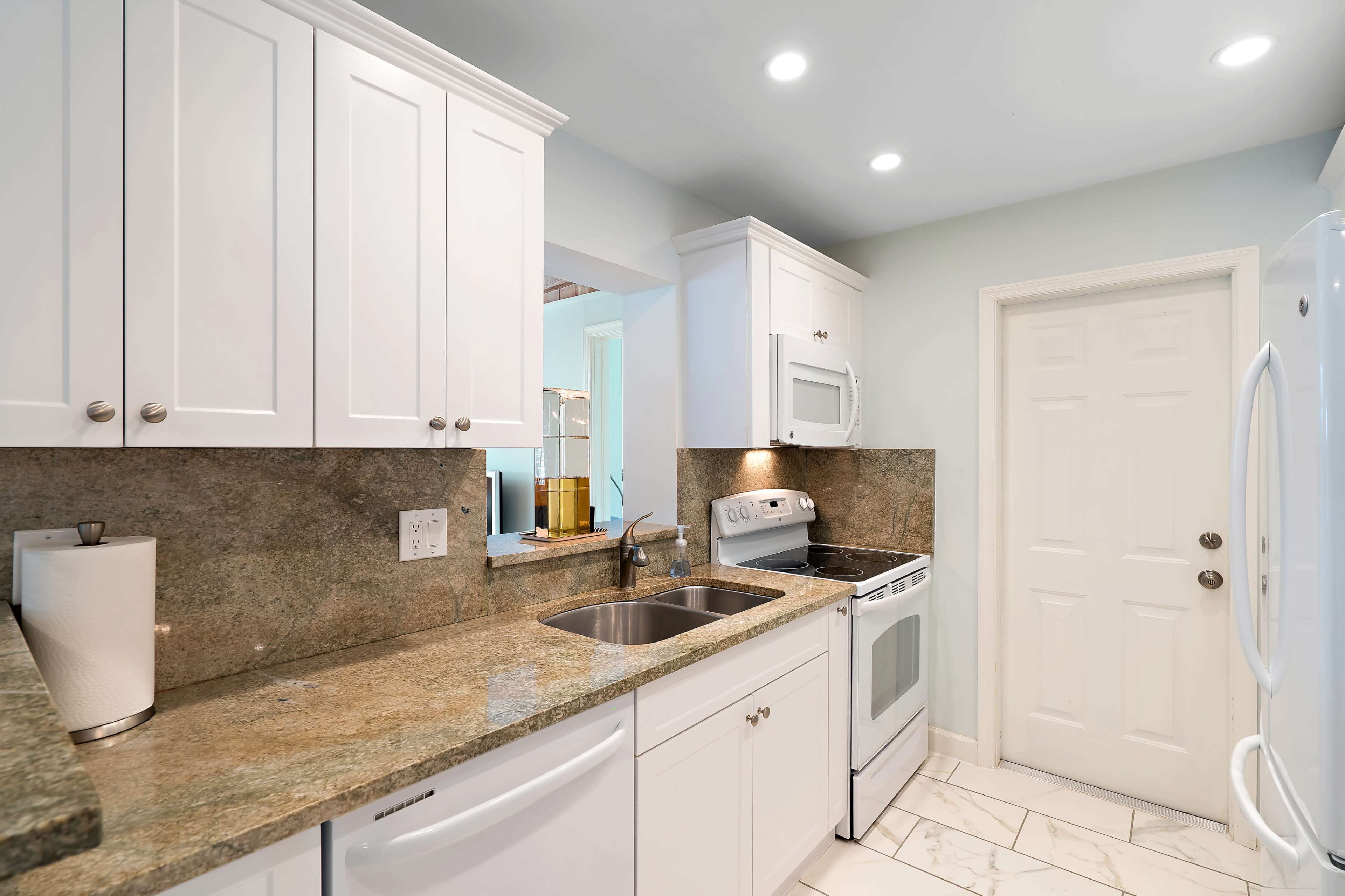 The image shows a modern kitchen featuring white cabinetry, granite countertops, and stainless steel appliances.