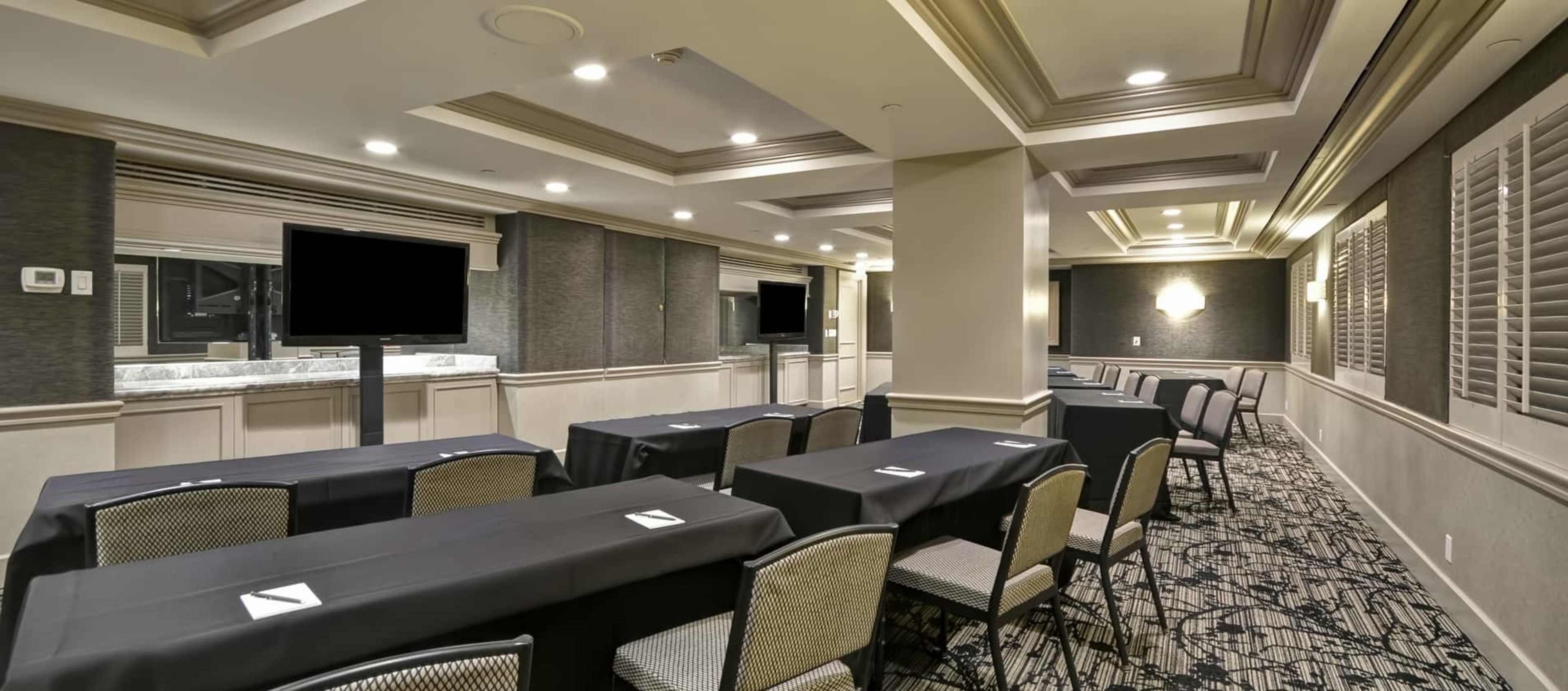 A conference room set up with several tables covered in black tablecloths and rows of chairs, illuminated by ceiling lights.
