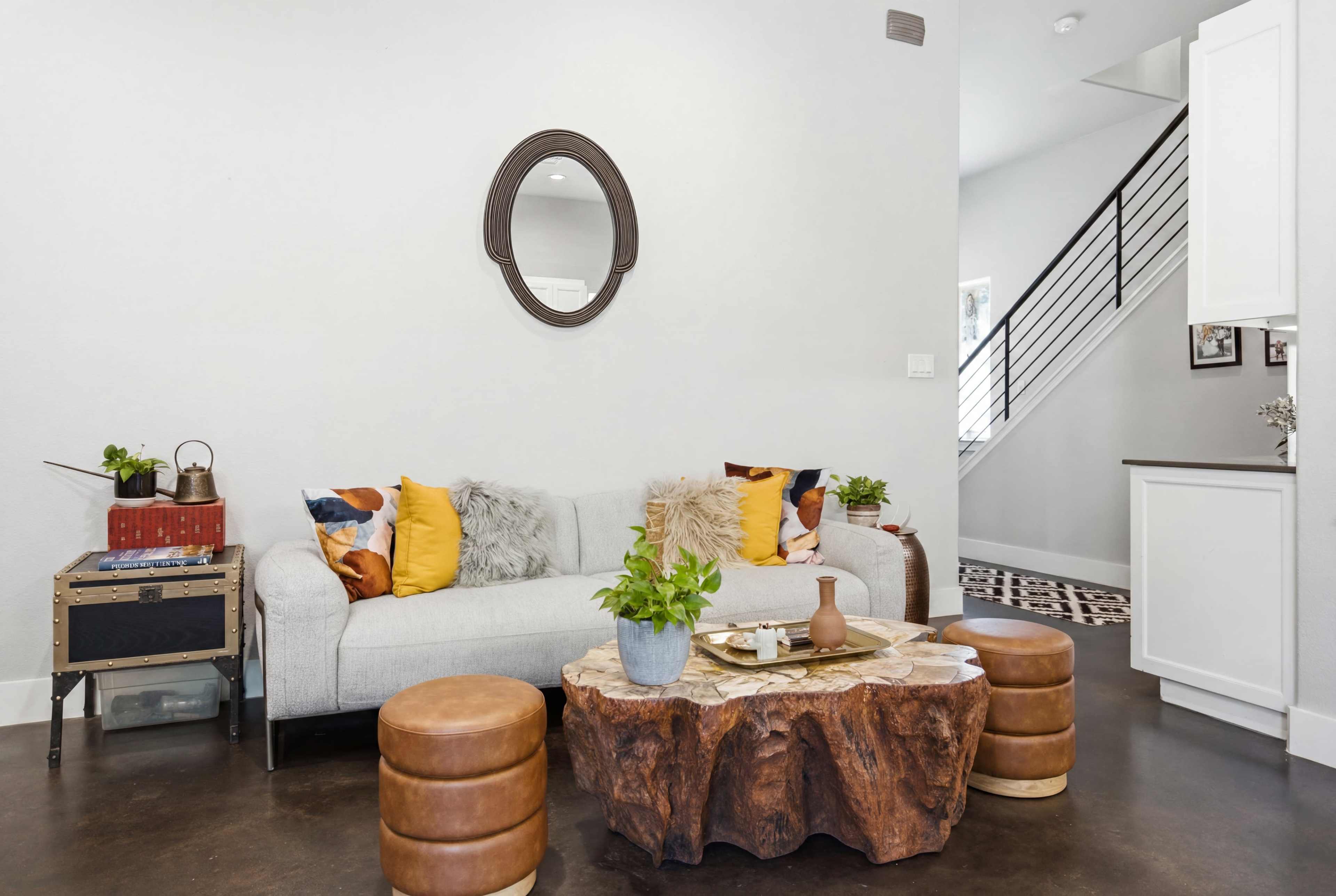 The image features a modern living room with a light-colored sofa adorned with colorful pillows, a wooden coffee table, and a staircase leading to another level.