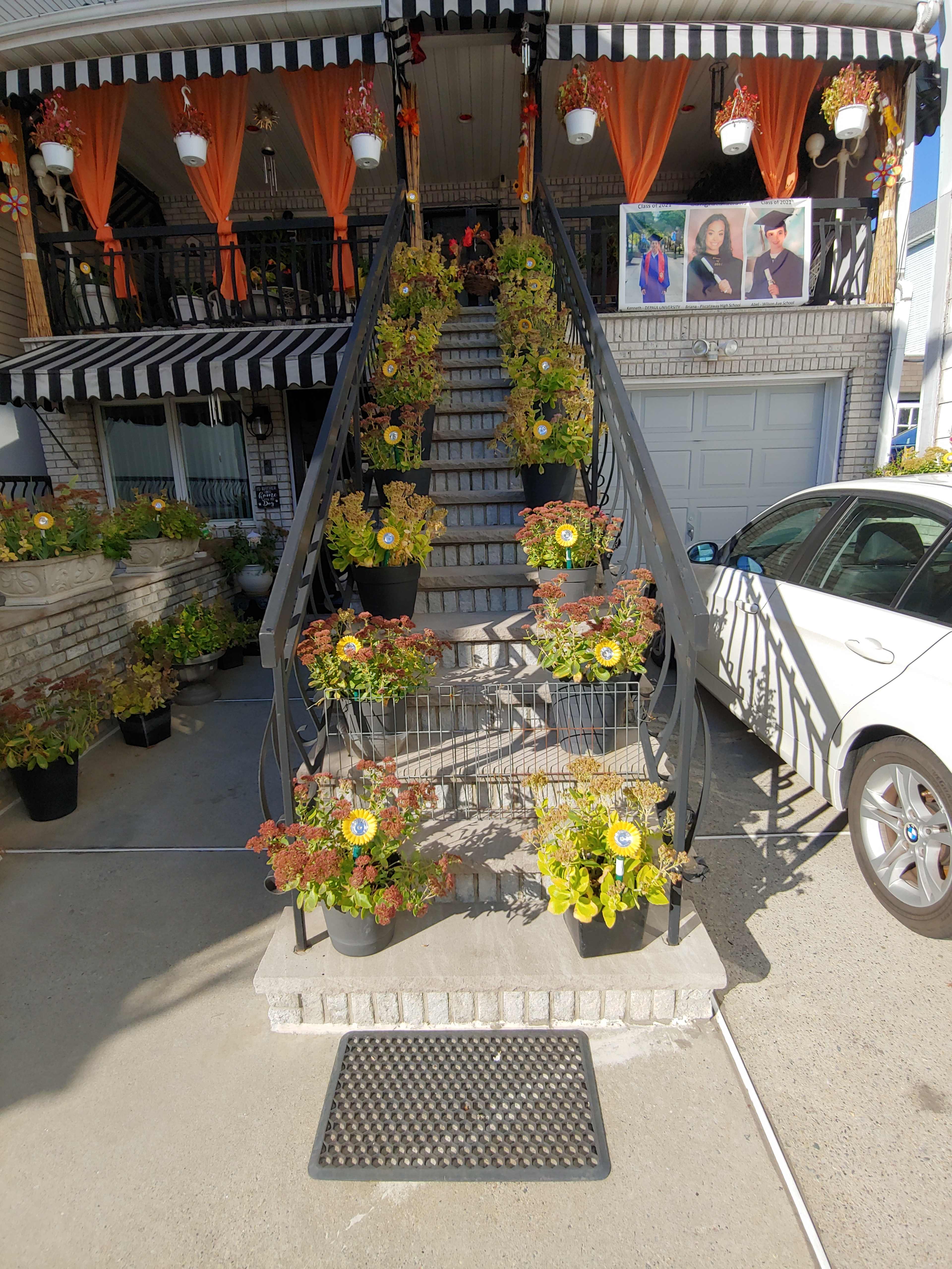 A staircase adorned with flower pots on each step, leading up to a house with a striped awning and decorative drapes.