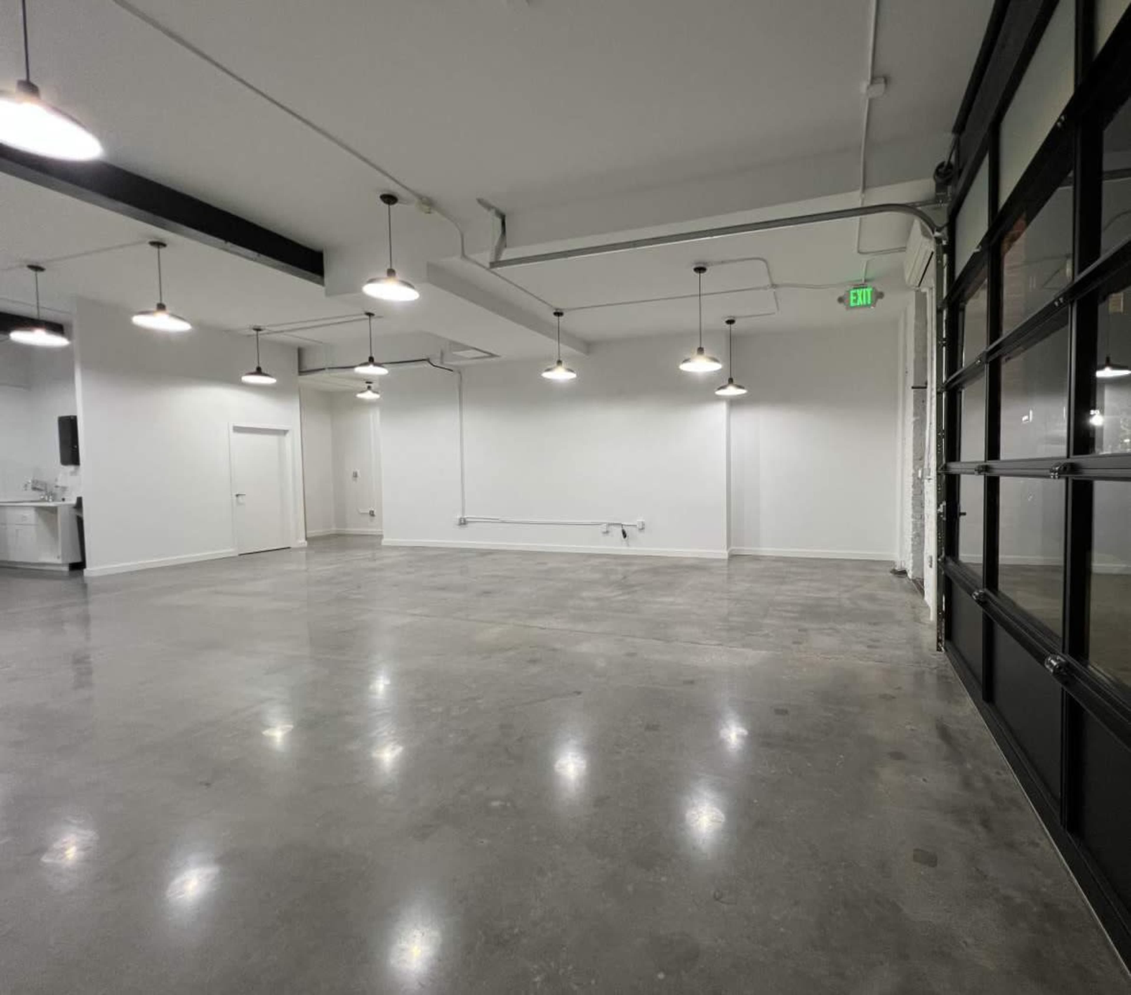 The image shows a spacious, empty room with polished concrete floors, overhead pendant lights, and a large glass door.