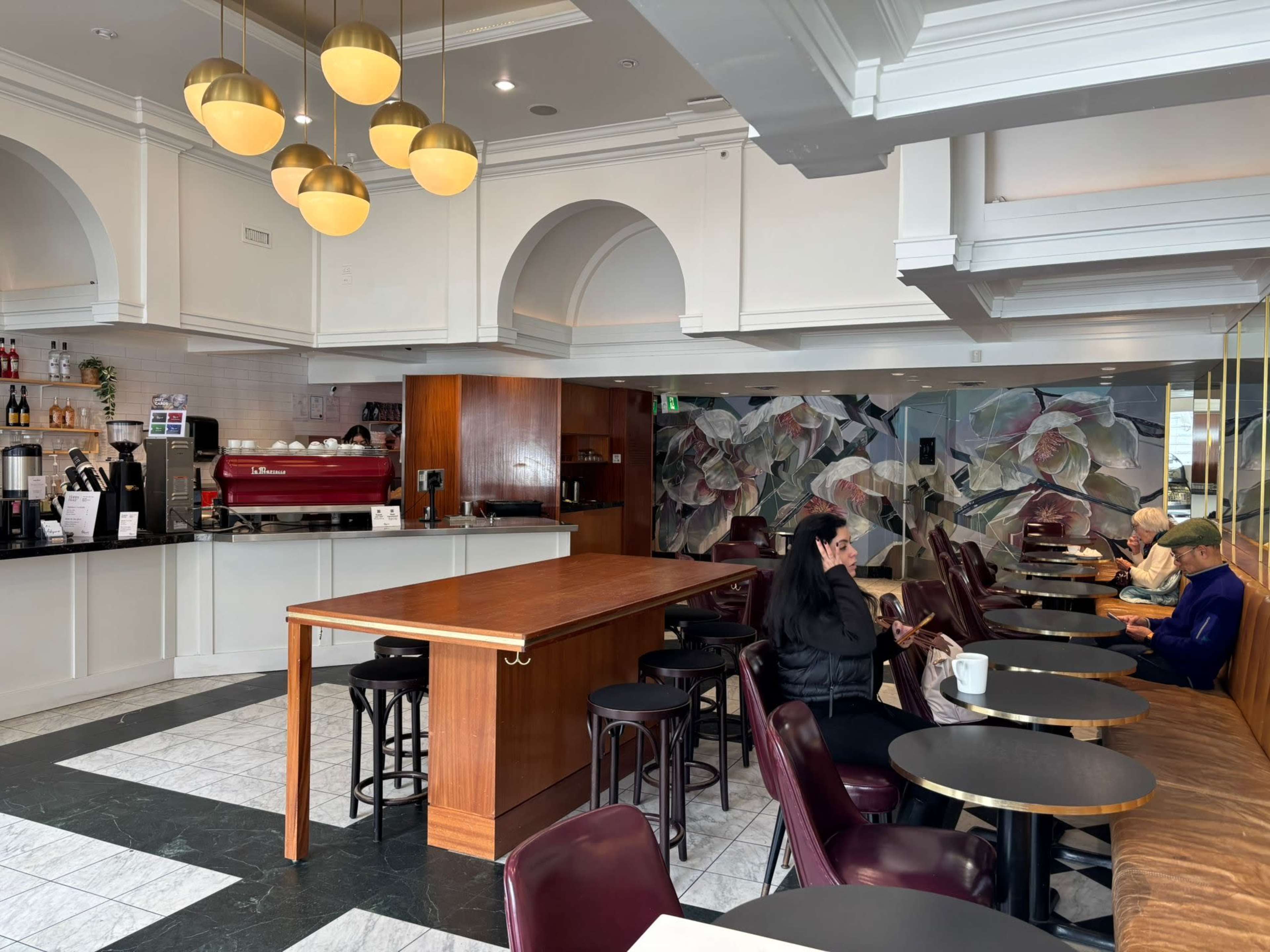 The image shows a modern café interior with a counter, seating area, and decorative wall mural.