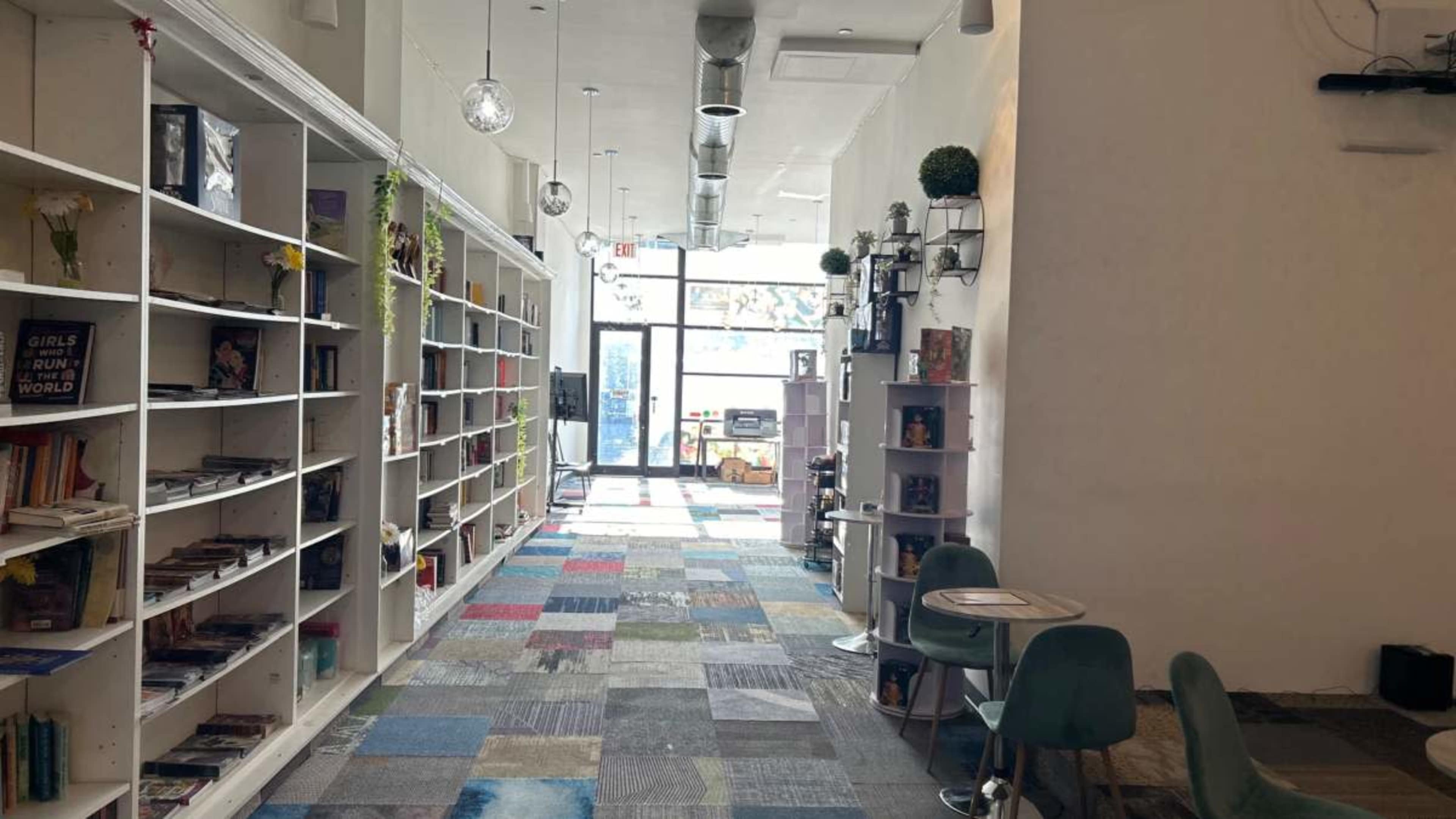 A spacious hallway lined with bookshelves on one side and colorful carpet tiles leading to a glass entrance at the far end.
