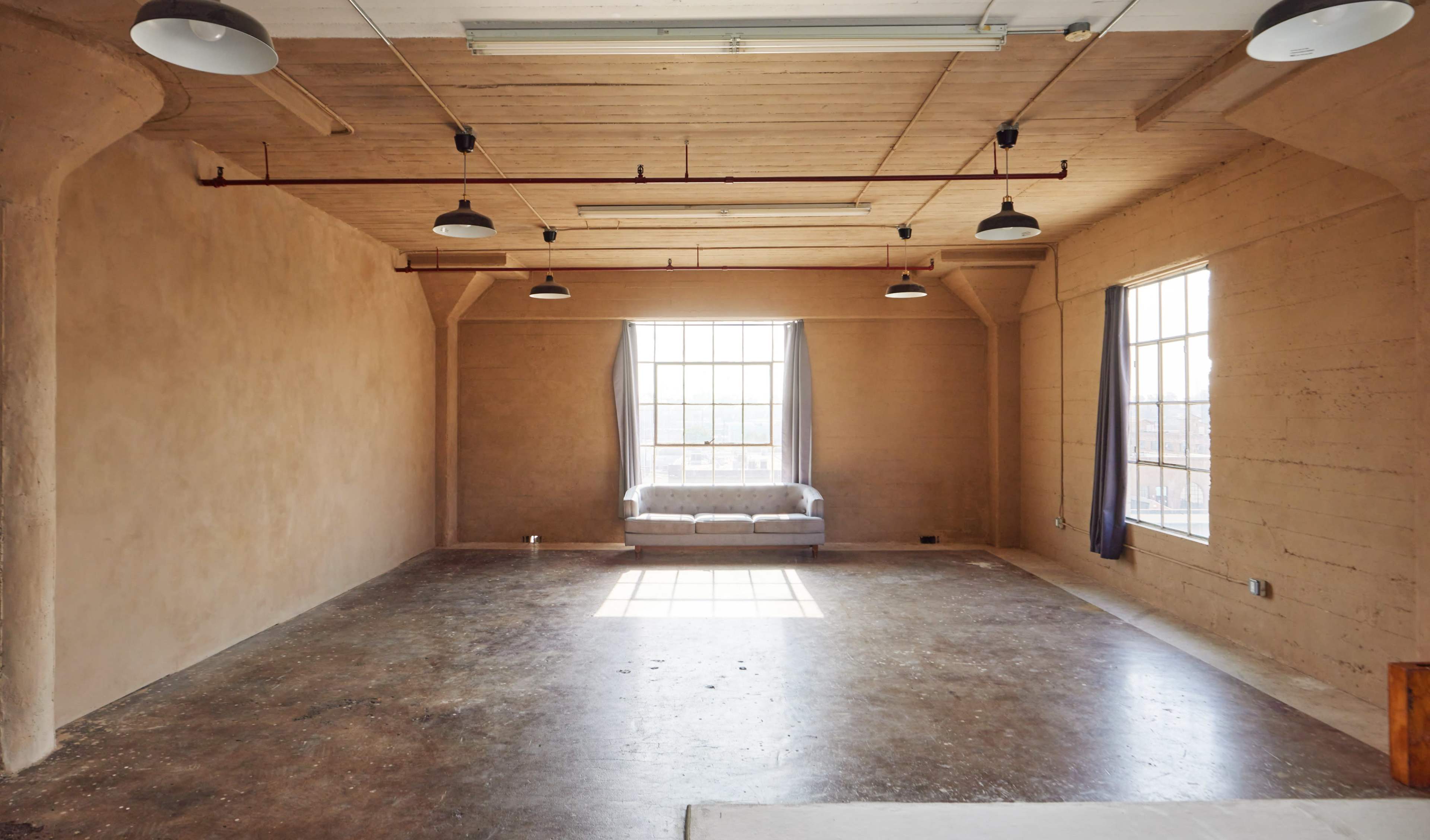 A spacious, empty room with a large window, a couch against one wall, and exposed roof beams.