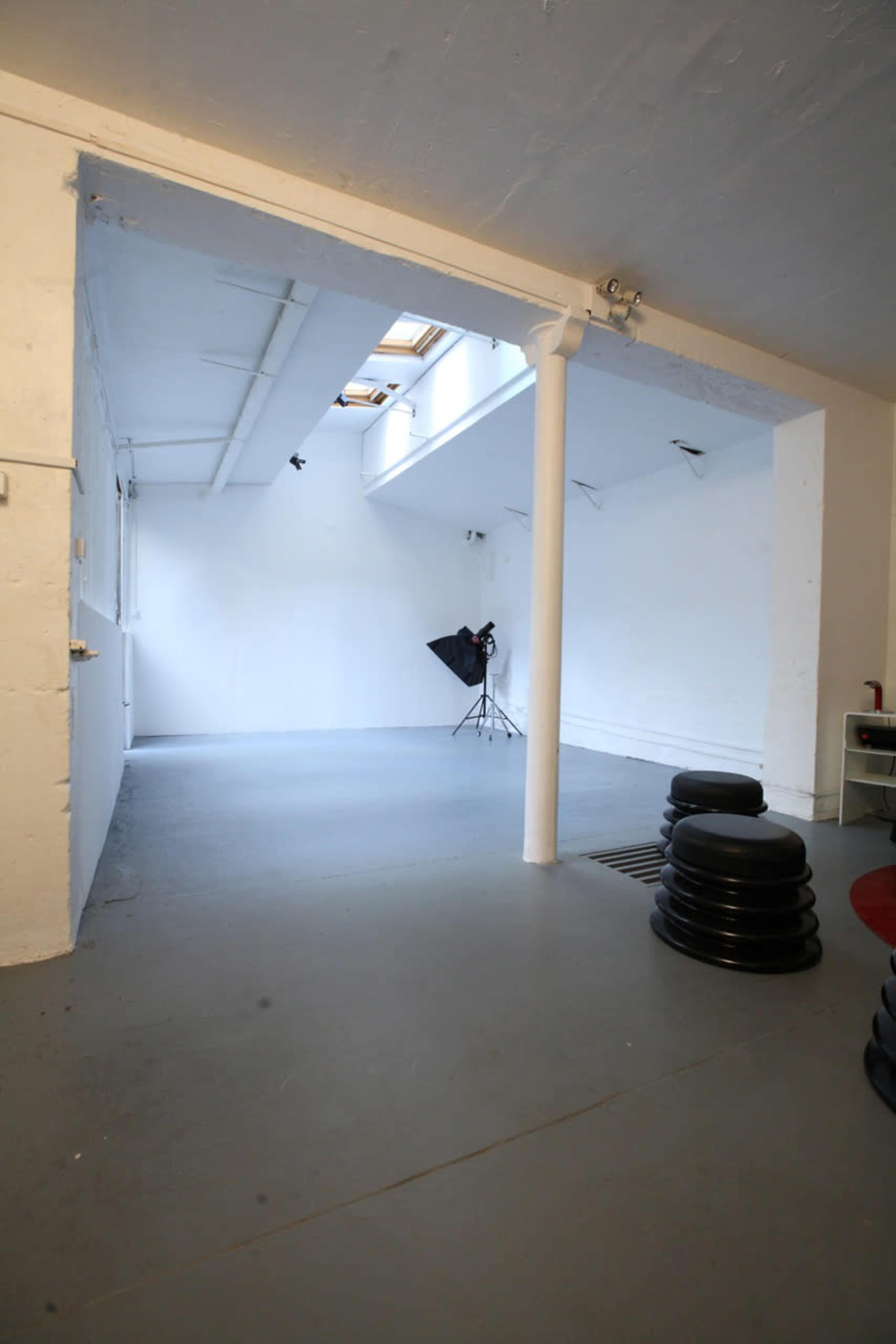 A spacious, well-lit studio with white walls, a gray floor, and a photography backdrop setup in one corner.