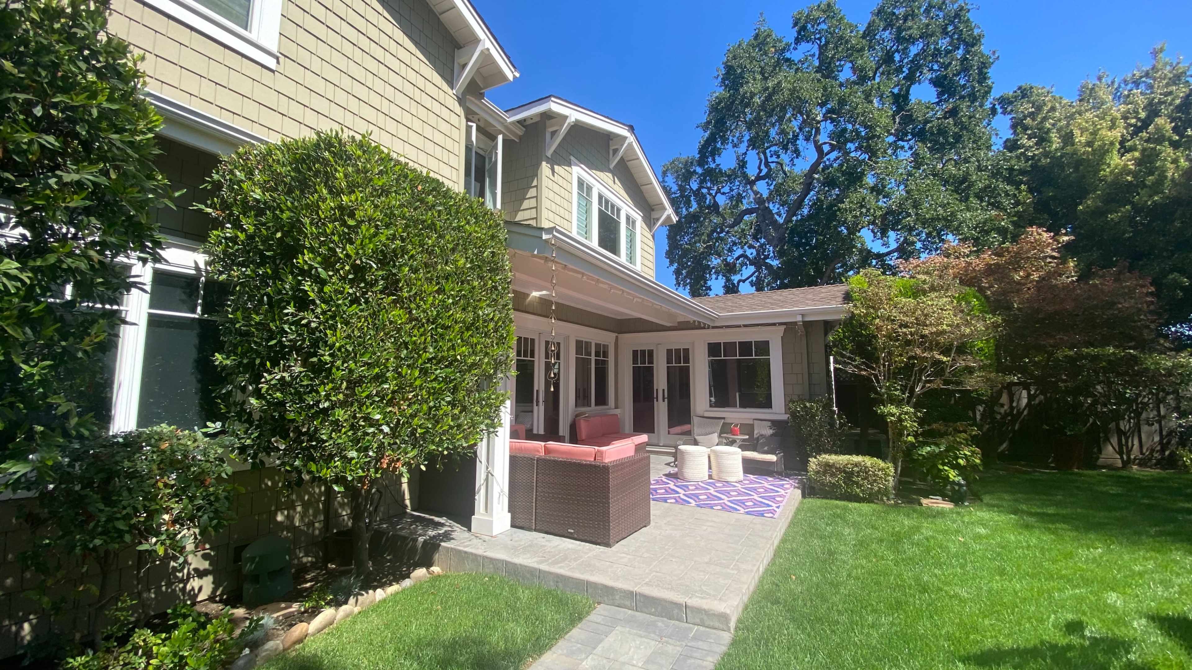 A well-maintained backyard features a patio with seating surrounded by lush greenery and trees.