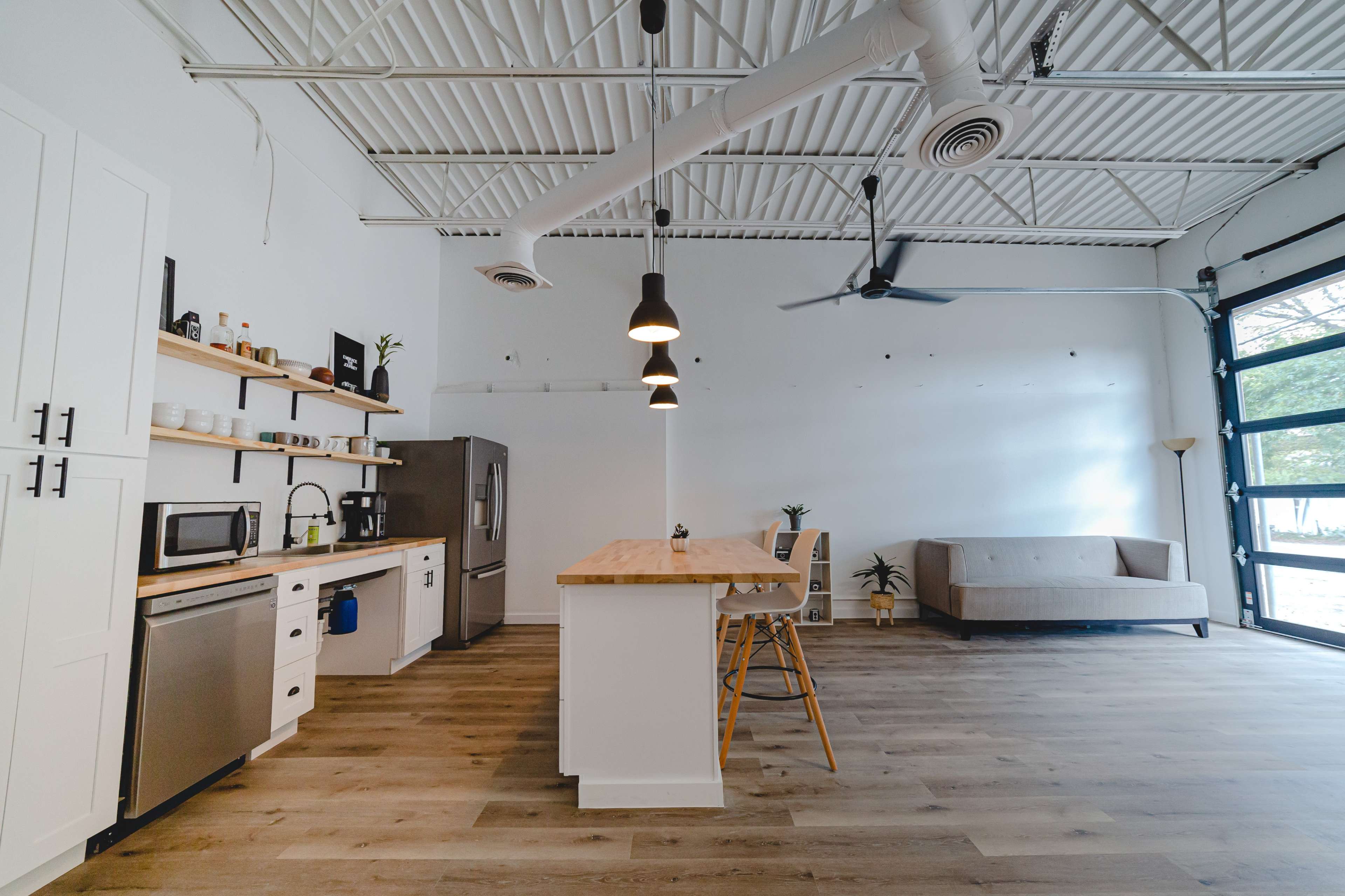 A modern, spacious kitchen and living area features a central wooden island, stainless steel appliances, and large windows leading to an outdoor view.