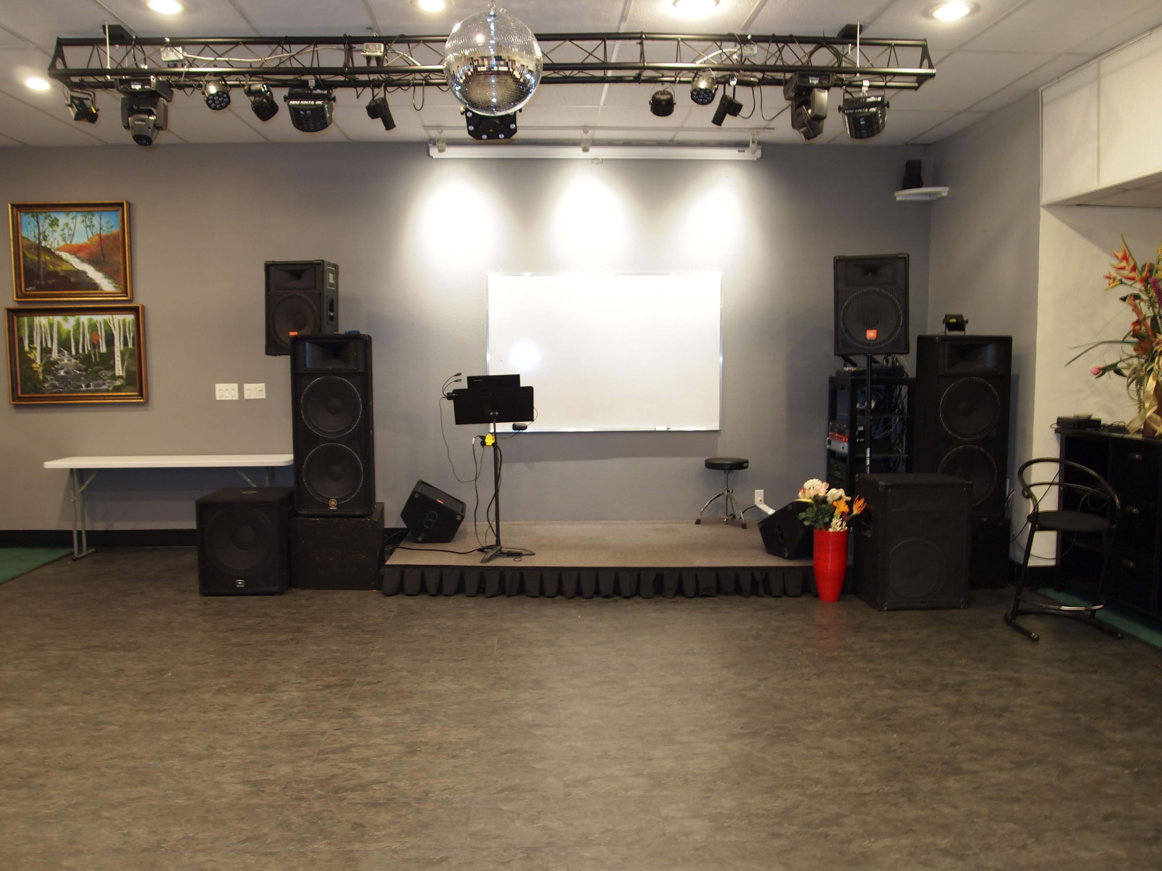 A stage setup in a room with a disco ball, large speakers, a monitor stand, and a blank whiteboard.